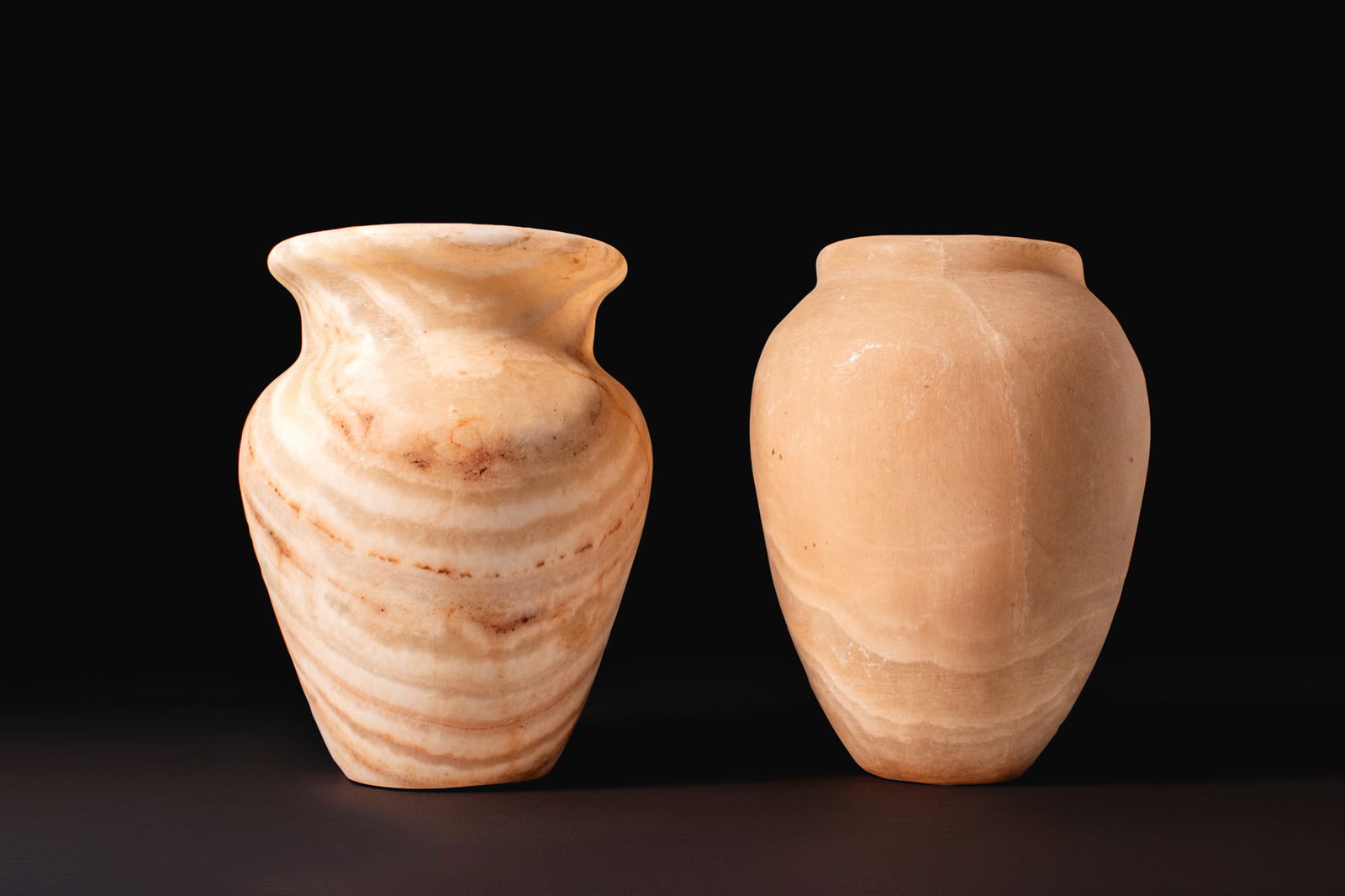 PAIR OF EGYPTIAN STONE VESSELS: Old Kingdom, Ca. 2640 - 2200 BCA pair of alabaster vessels, including, from left to right: a jar with a piriform body and funnel-shaped neck with everted rim; and a jar with a tapering ovoid body and