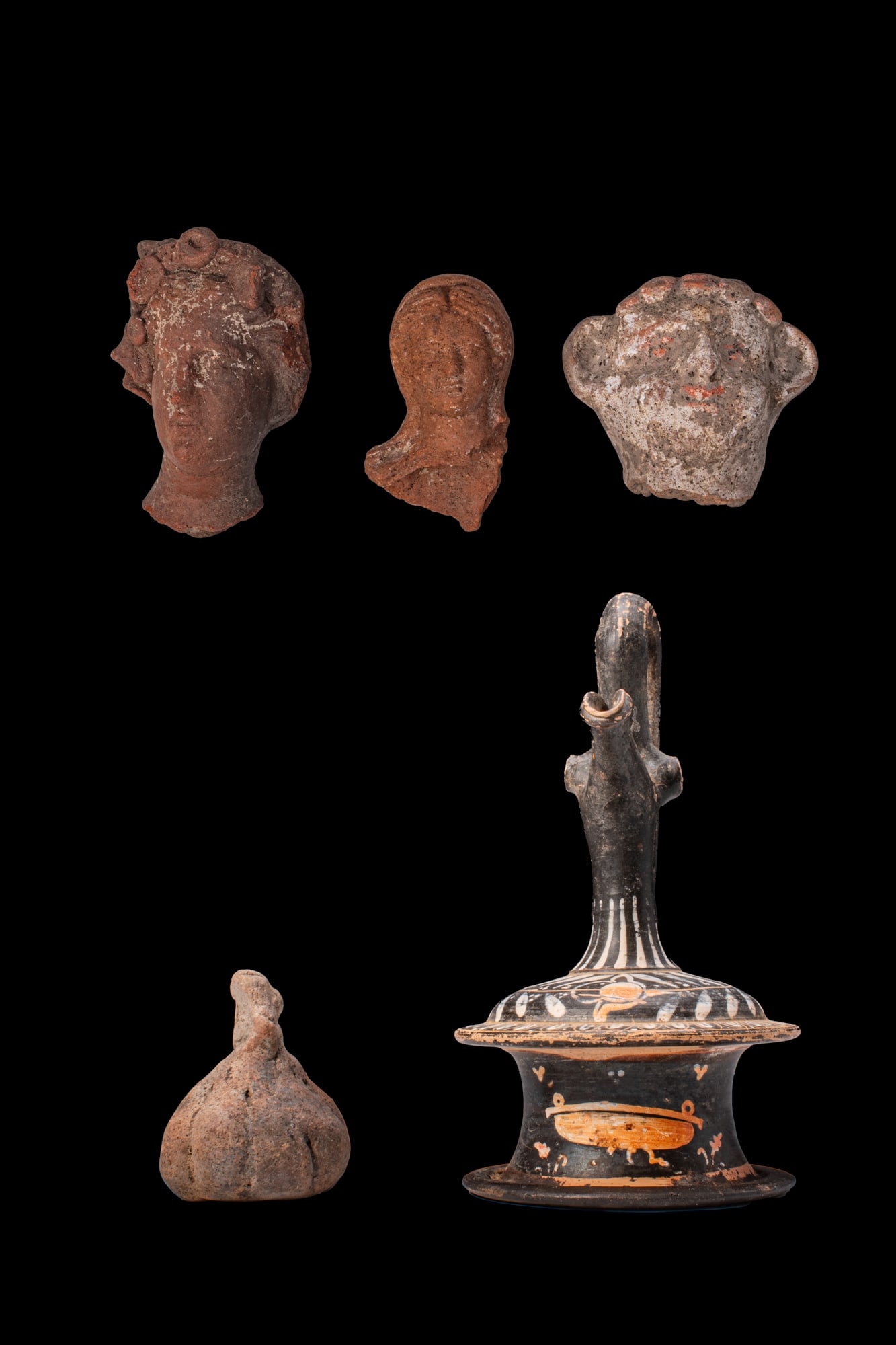 COLLECTION OF HELLENISTIC TERRACOTTA HEADS AND GNATHIAN EPICHISIS: Ca. 400 - 200 BC A collection of five objects, including, from left to right: three moulded terracotta heads, the first with a rolled coiffure; the second with an oval face and centrally parted hair