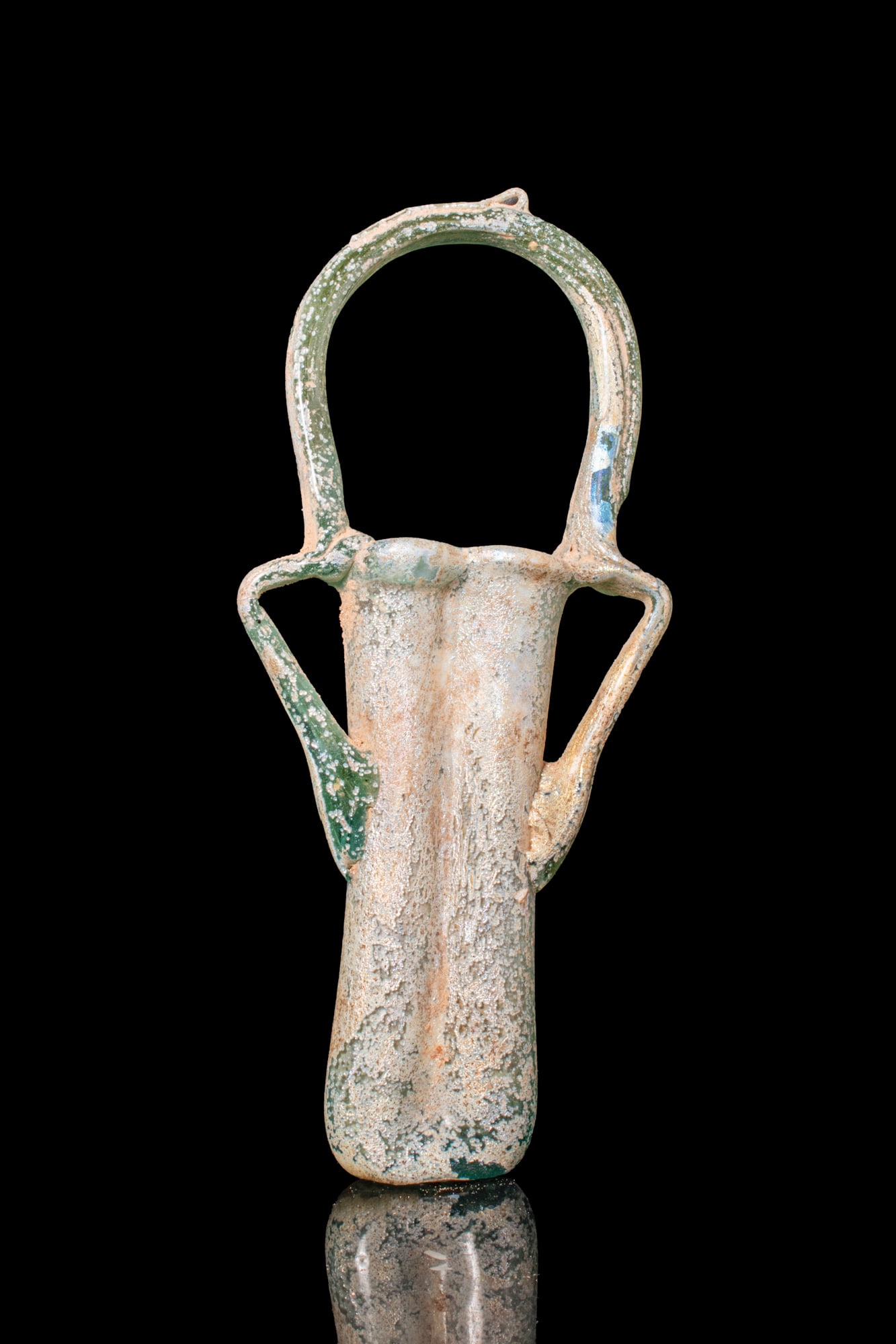 ROMAN GLASS DOUBLE BALSAMARIUM WITH HANDLE: Ca. AD 300A pale green translucent glass double balsamarium composed of two elongated tubular vials joined along their long sides. From the shoulders, an applied trail is drawn up and folded at the ri
