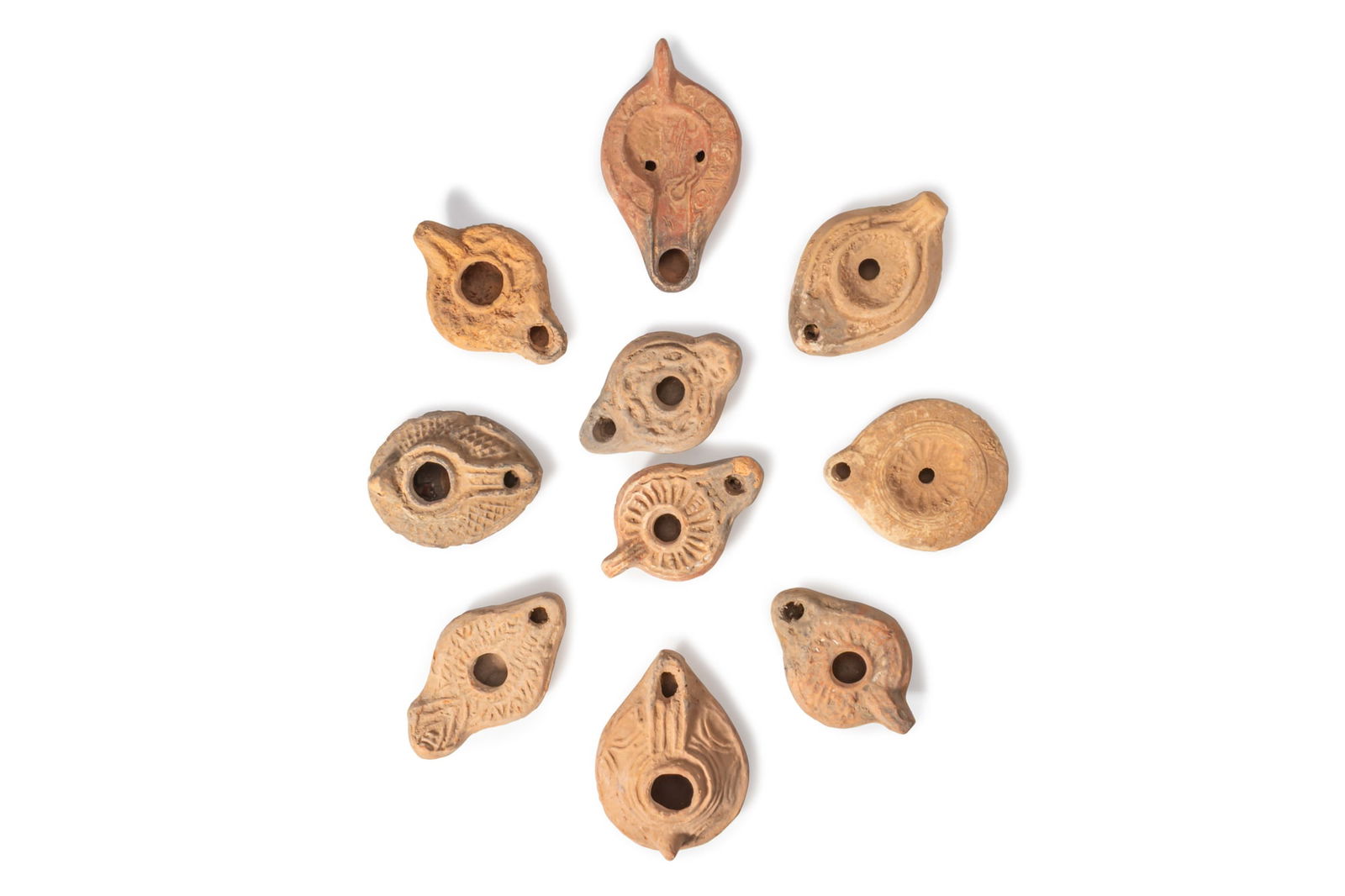 COLLECTION OF ROMAN AND BYZANTINE TERRACOTTA OIL LAMPS: Ca. AD 200 - 600A collection of ten terracotta oil lamps, each with a drop-shaped or circular body and a recessed central filling hole within a raised rim. The shoulders have moulded decoration,
