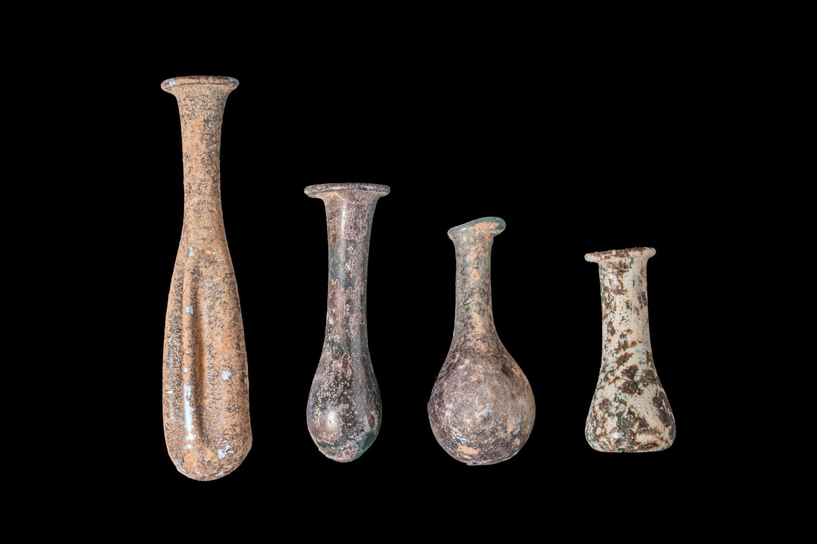 COLLECTION OF ROMAN GLASS UNGUENTARIA: Ca. AD 300 - 400A collection of four glass unguentaria, including, from left to right: a free-blown bottle with a long fluted lower body; a green vial with a slender cylindrical neck and elongated