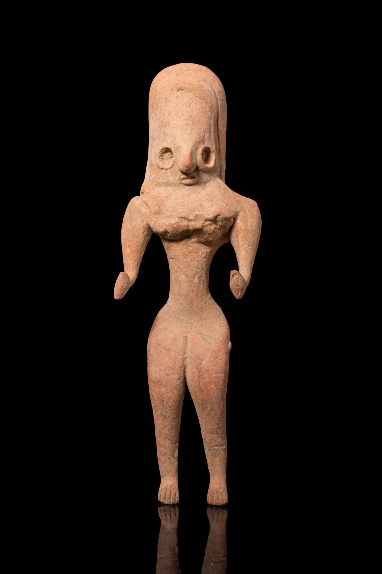 INDUS VALLEY TERRACOTTA FERTILITY IDOL: Ca. 2500 BCA hand-modelled terracotta female fertility idol seated with the legs set apart, the elongated head with a high arching headpiece framing a stylised face with deep recessed eyes and hooked