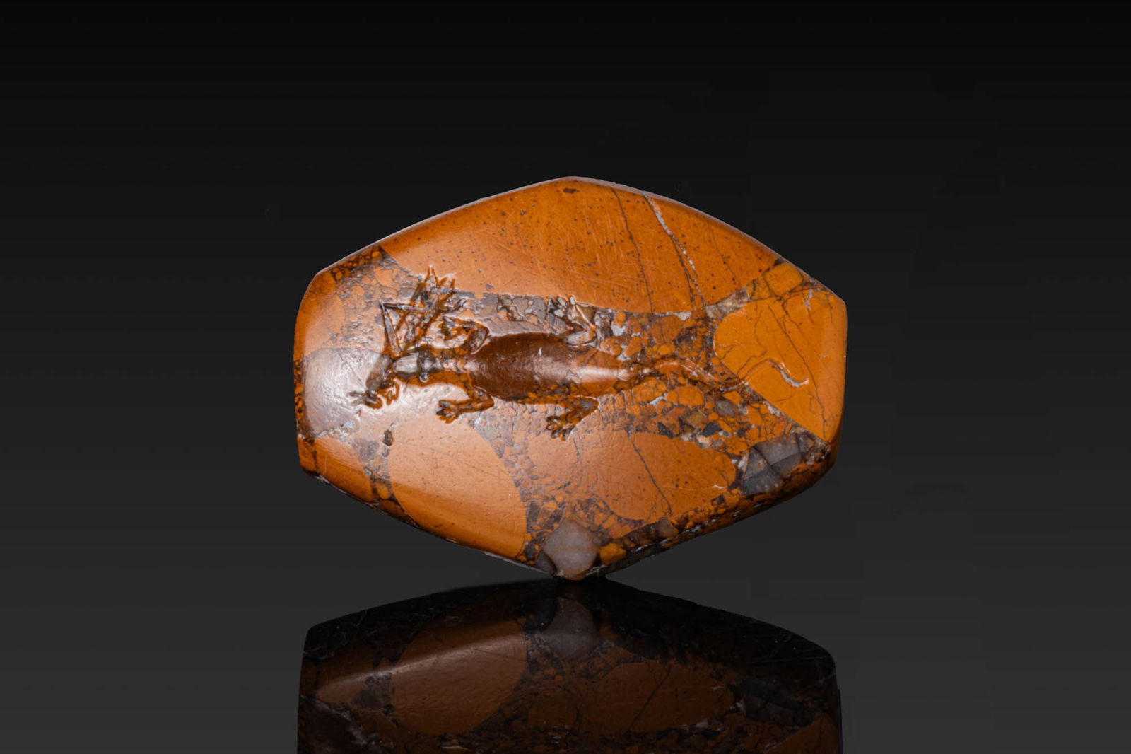 MINOAN BRECCIA STONE INTAGLIO OF A LIZARD EATING A GRASSHOPPER: Ca. 1600 - 1450 BC. A Late Minoan lentoid bead-seal of brecciated orange jasper, pierced longitudinally. One face is engraved with a lizard advancing left, its jaws closed on a grasshopper. For simila