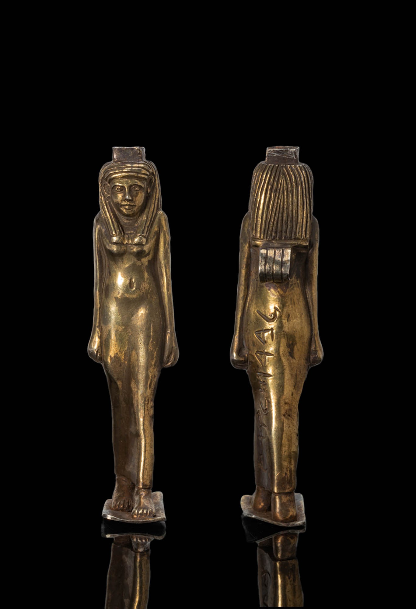 LARGE PHOENICIAN HIGH KARAT GOLD PENDANT OF ISIS WITH INSCRIPTION: Ca. 600 - 400 BC. A gold pendant of Isis standing on a rectangular base with the left leg advanced, the body in a close-fitting dress and the arms held at the sides. The head is framed by a tripartite