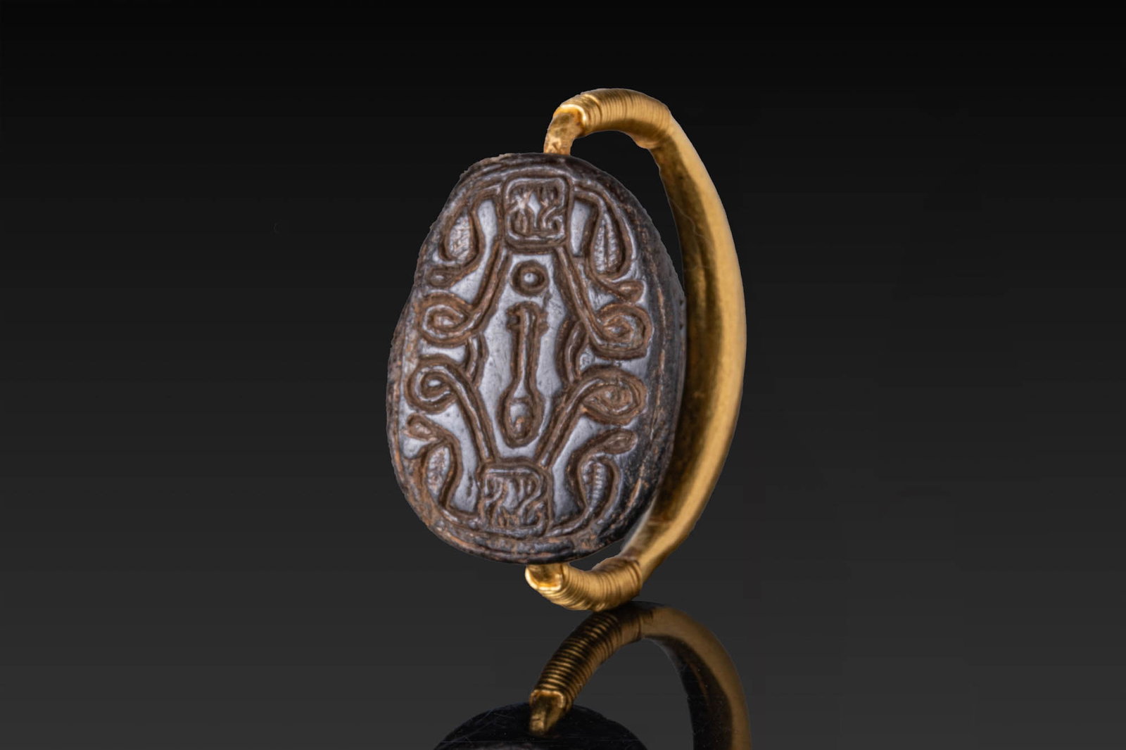 EGYPTIAN HIGH KARAT GOLD SWIVEL RING WITH ENGRAVED SCARAB: Middle Kingdom to Third Intermediate Period, Ca. 2055 - 1550 BC. A gold swivel ring with a thick, rounded hoop, the shoulders wrapped with fine coiled wire supporting a rotating scarab. The base is ca