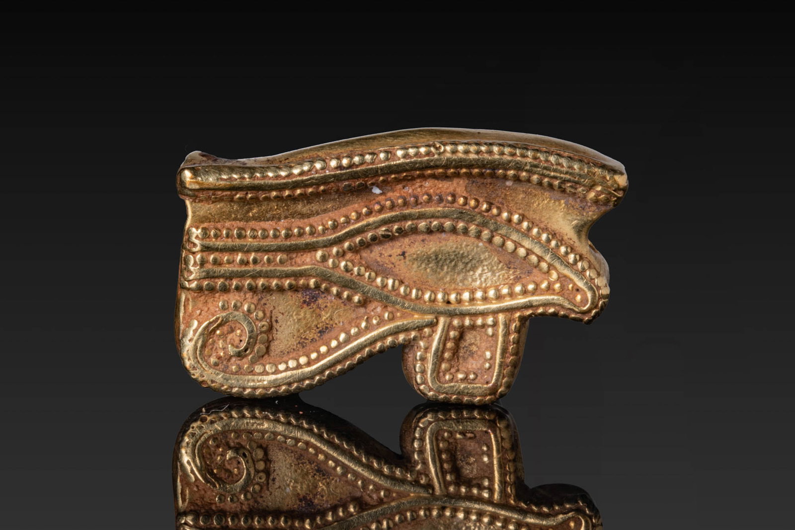 RARE EGYPTIAN HIGH KARAT GOLD EYE OF HORUS AMULET: Late Period, Ca. 664 - 332 BC. A gold Eye of Horus amulet formed as a stylised eye with dotted detailing along the brow and lid, the cosmetic line, and the markings beneath the eye, perforated transve