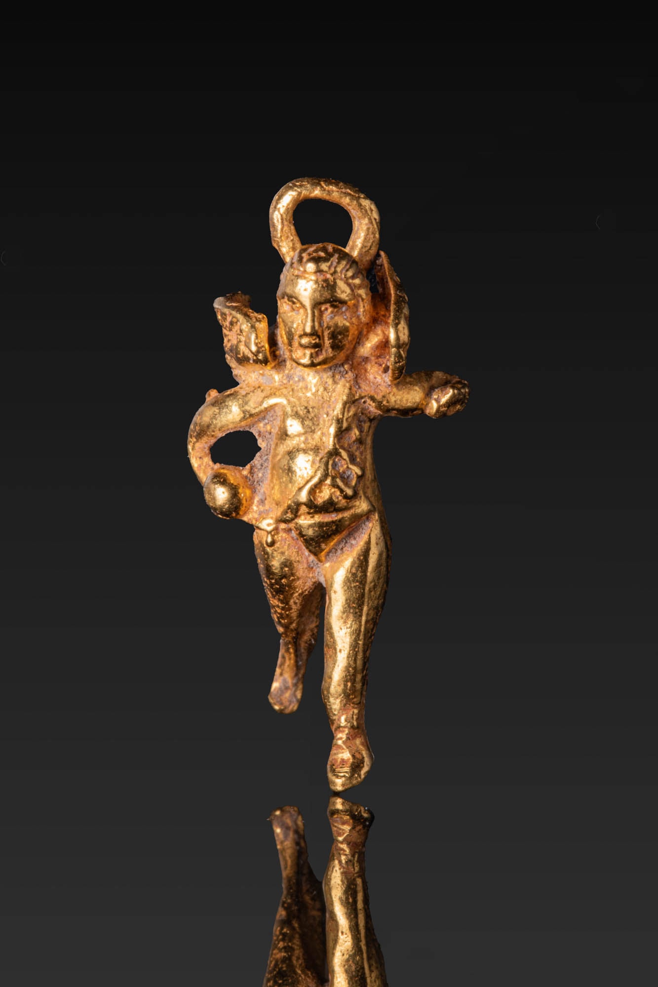 HELLENISTIC HIGH KARAT GOLD PENDANT OF EROS: Ca. 400 - 300 BC. A gold pendant in the form of Eros, modelled in the round with arms outstretched and the left leg advanced, the wings with incised feathers and a quiver slung diagonally across the c