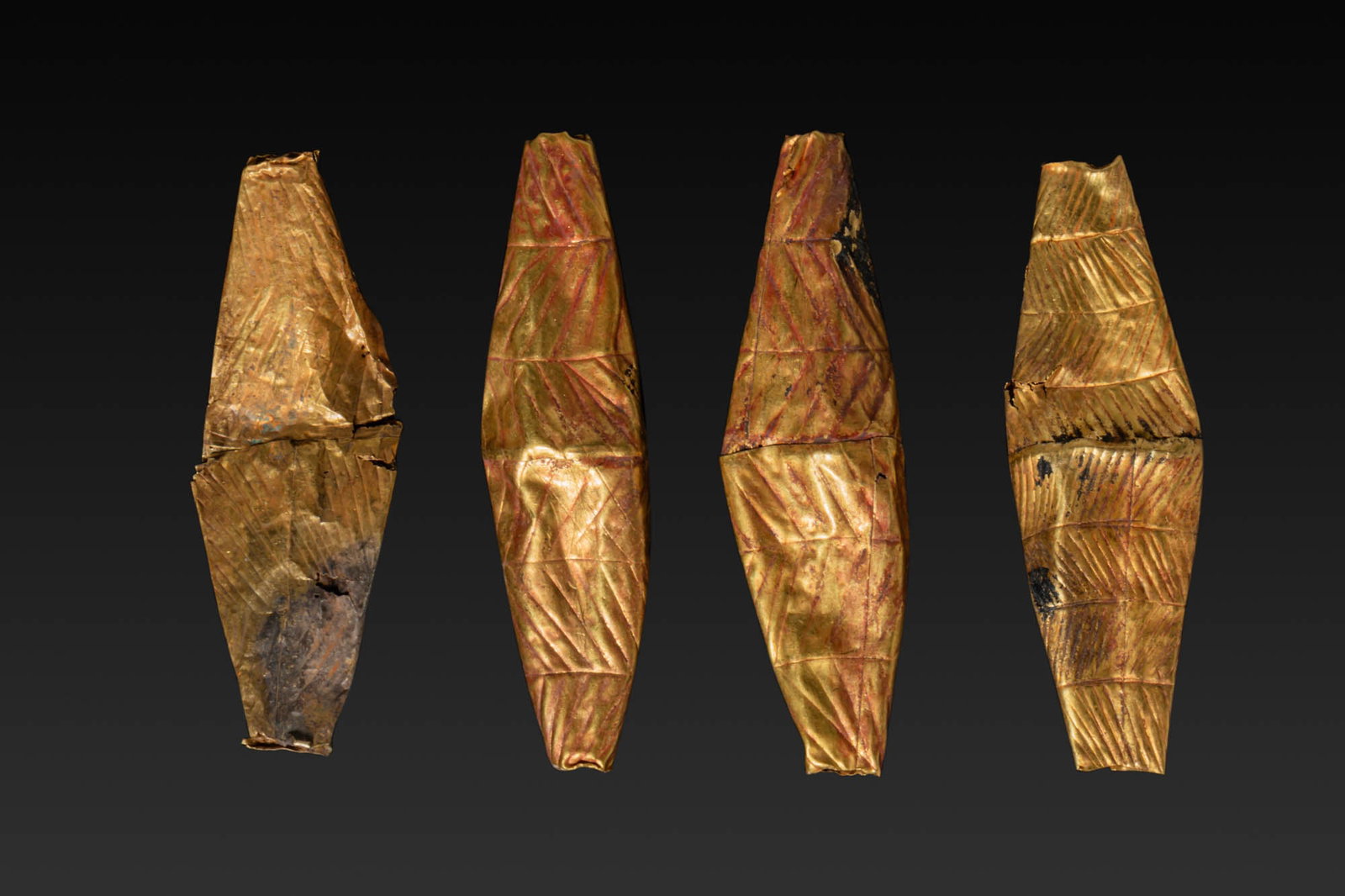 COLLECTION OF FOUR LARGE GREEK GEOMETRIC HIGH KARAT GOLD BICONICAL BEADS WITH ENGRAVED MOTIFS: Ca. 800 - 600 BC. A collection of four gold beads, each formed as an elongated biconical element made from a thin sheet, with the surface divided into parallel registers and decorated with diagonal ha