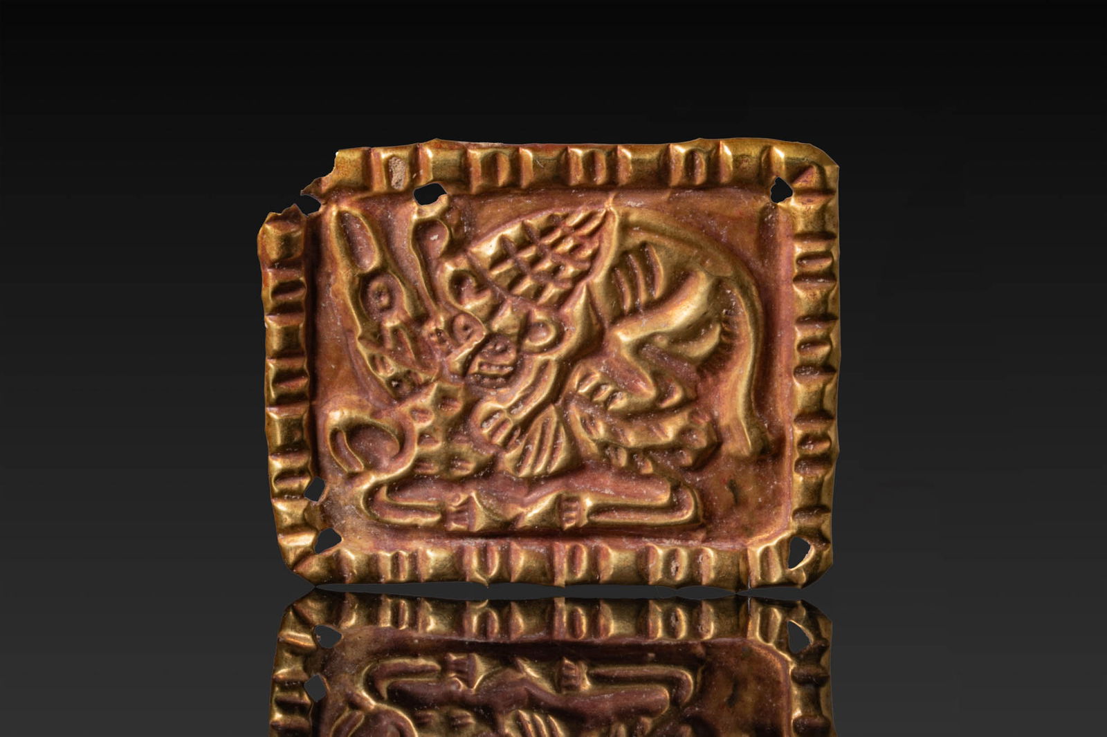 SCYTHIAN REPOUSSE HIGH KARAT GOLD PLAQUE WITH LION AND DEER: Ca. mid-1st millennium BC. A repouss? gold plaque depicting a lion attacking a deer within a recessed rectangular field, framed by a raised border with corner perforations for attachment. Size: 37mm x