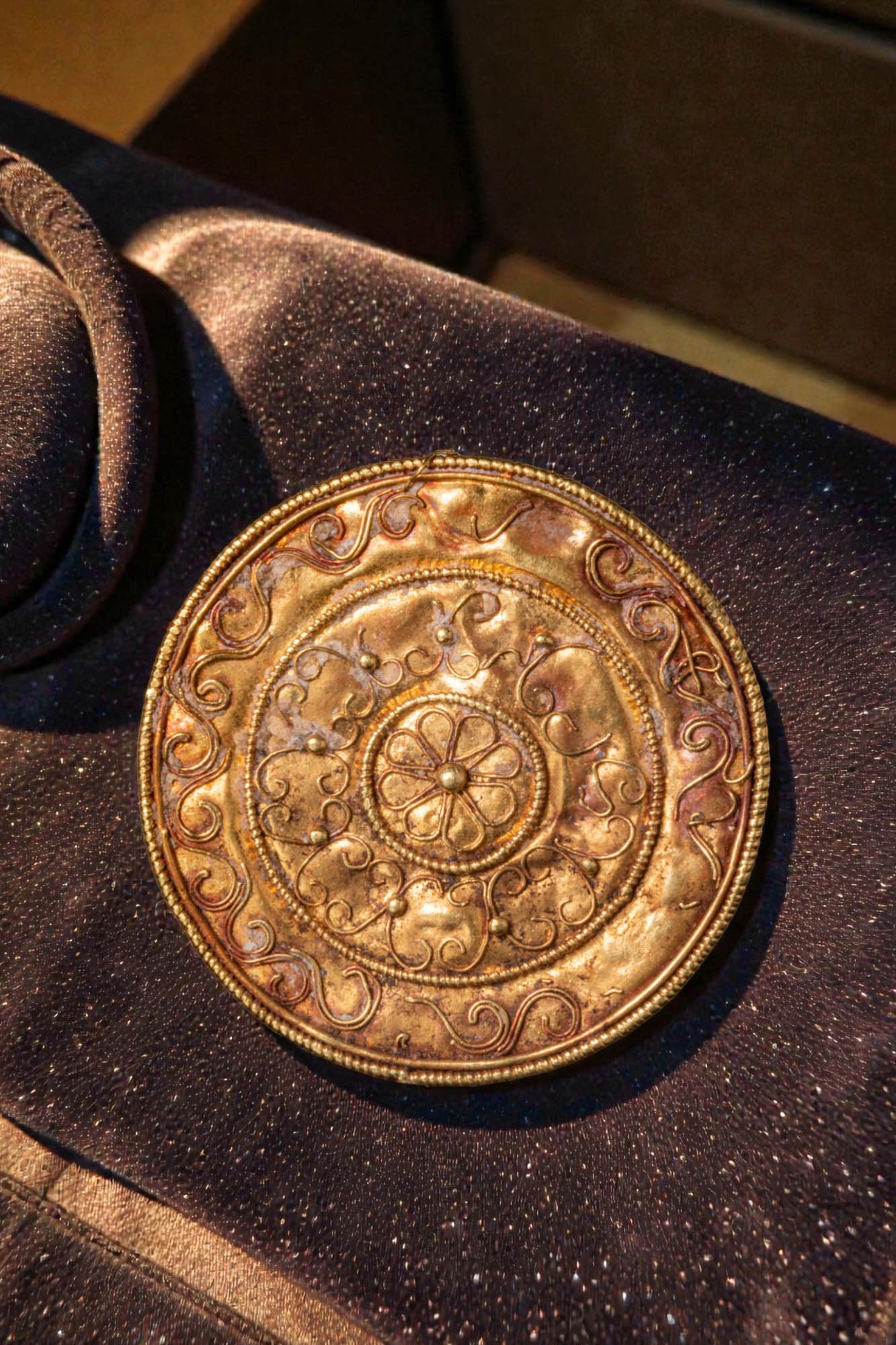 BEAUTIFUL HELLENISTIC HIGH KARAT GOLD DISC APPLIQU? WITH ROSETTE: Ca. 300 - 100 BC. A gold circular appliqu? centred by a rosette within concentric registers of scrolling filigree ornament, finished at the edge with a beaded rim, the reverse with an attachment loop.