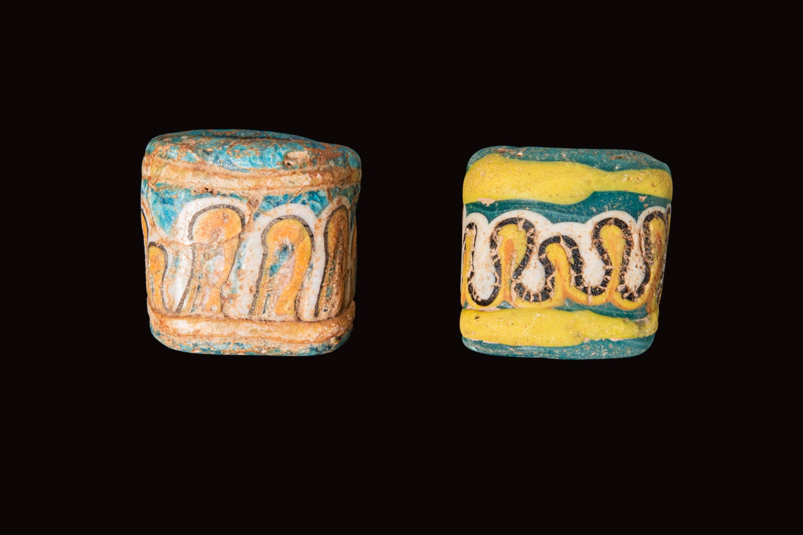 PHOENICIAN GLASS BEADS WITH WAVE MOTIF: Ca. 600 - 400 BC. A pair of glass cylindrical beads, each a turquoise bead with an applied undulating wave motif in white, yellow, orange and black, set between horizontal bands. For similar see: The