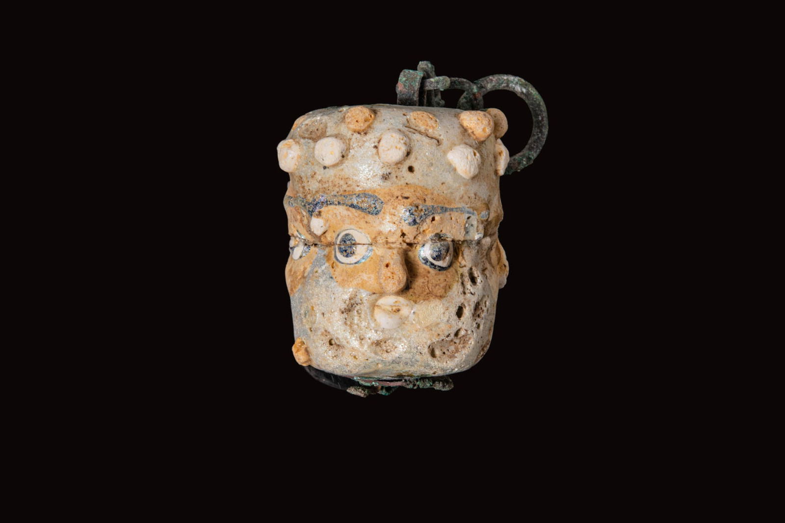 LARGE PHOENICIAN GLASS FACE BEAD WITH A BRONZE CHAIN: Ca. 500 - 400 BC. A large glass bead of cylindrical form with three faces spaced around the circumference, each with a prominent nose and eyes with blue pupils, the remaining field with two rows of ap