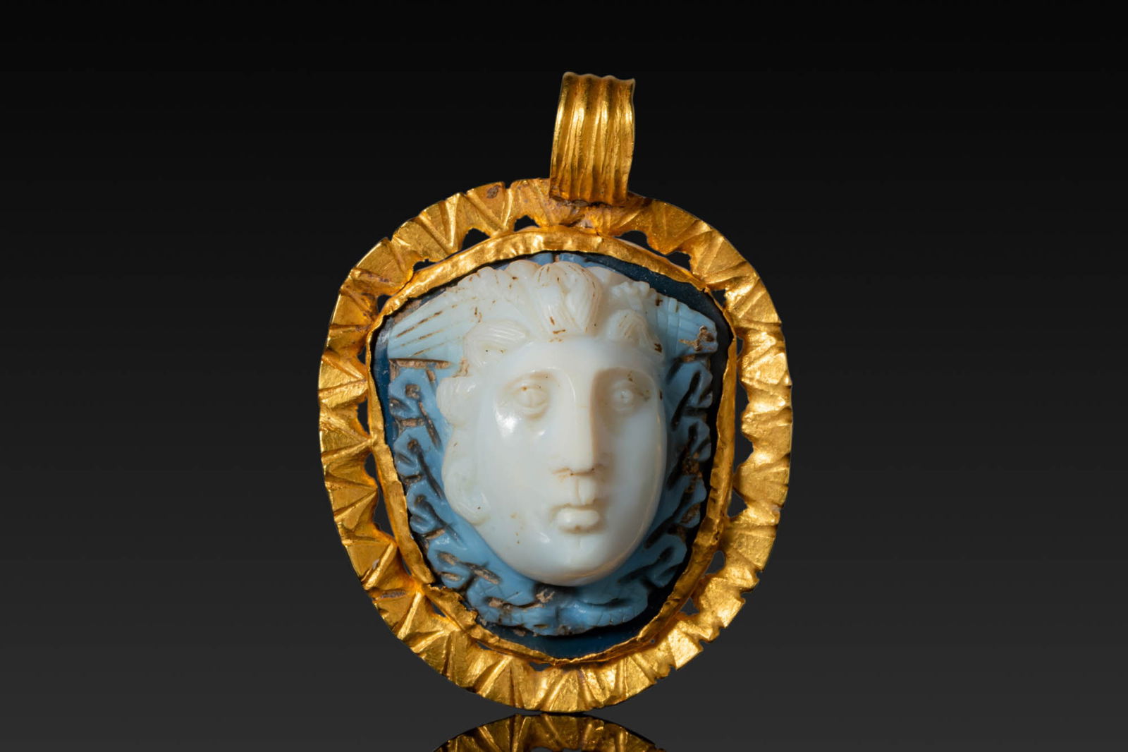 ROMAN AGATE CAMEO OF MEDUSA IN A HIGH KARAT GOLD FRAME: Ca. AD 200 - 300. An agate cameo carved in high relief as the head of Medusa, shown frontally with prominent eyes, a straight nose and a small mouth, the hair arranged in radiating locks with carved s