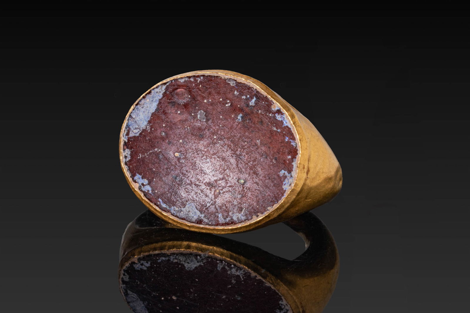 LARGE ROMAN HIGH KARAT GOLD RING WITH GLASS BEZEL: Ca. AD 1 - 300. A gold ring with a broad oval bezel plate, the plain rim forming a shallow frame for a glass insert, on tapering shoulders and a plain hoop of rounded section. Size: D:15.29mm / US: 4