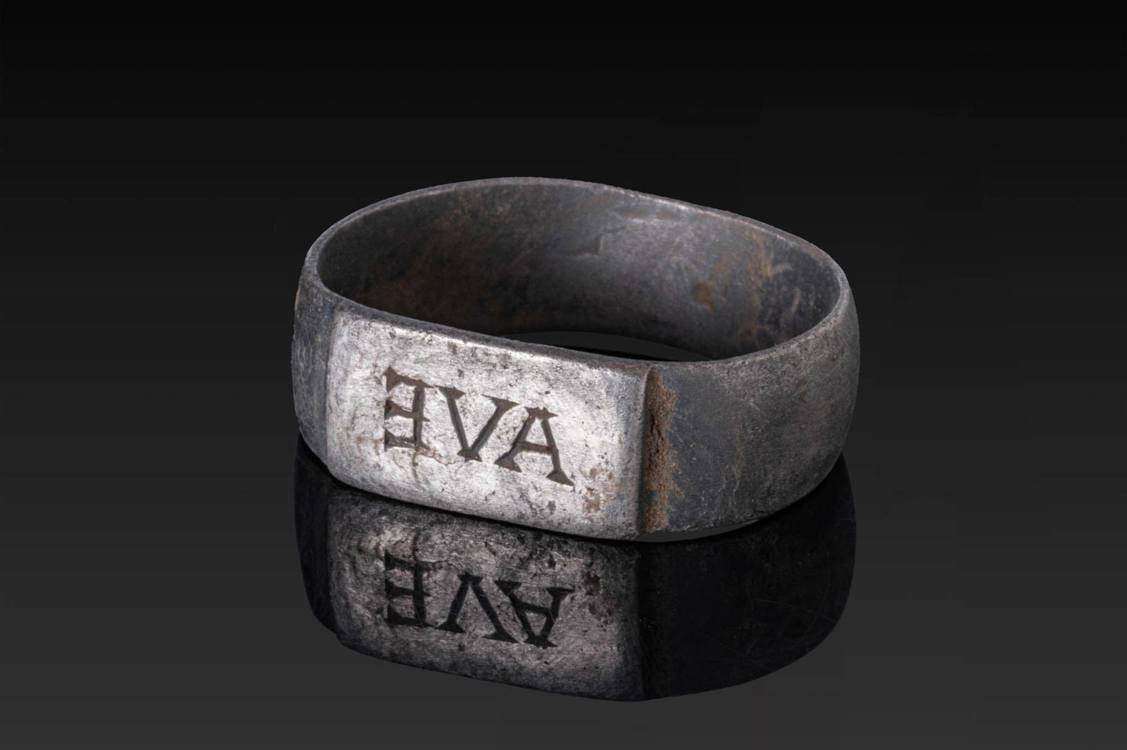 ROMAN SILVER RING WITH LATIN INSCRIPTION 'AVE': Ca. AD 1 - 200. A silver ring formed as a broad flat-section hoop with a rectangular bezel plate engraved with the retrograde Latin inscription 'AVE' in serifed capitals. Size: D:19.56mm / US: 9 3/4 /