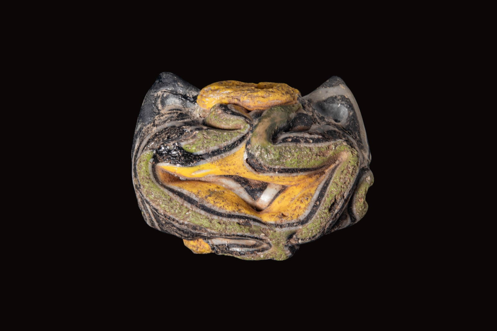 LATE ROMAN POLYCHROME GLASS BEAD: Ca. AD 200 - 400. A polychrome glass bead of barrel form with a central perforation, the black ground overlaid with marvered trails in white, yellow and green, forming sinuous bands around the circumf