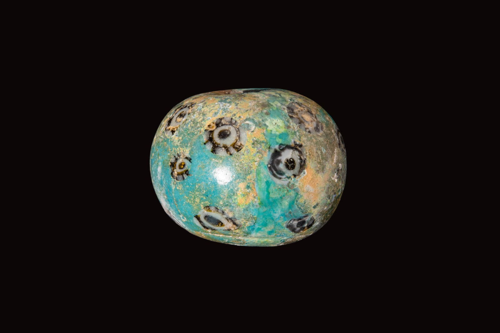 ROMAN MOSAIC GLASS BEAD WITH ROSETTES: Ca. 100 BC - AD 100. A mosaic glass bead of globular form with a central perforation, the turquoise ground set with dispersed rosette canes in white and dark glass. Size: 37mm x 29mm; Weight: 52g Prov