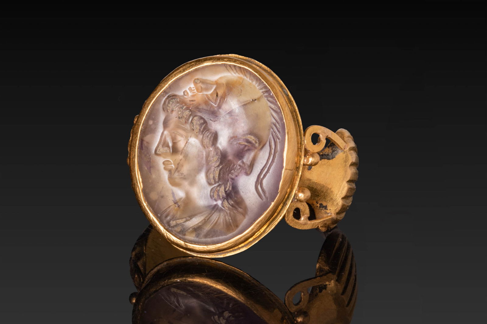 ROMAN AMETHYST INTAGLIO OF MINERVA WITH A DOUBLE-HEADED HELMET IN HIGH KARAT GOLD RING: Ca. 100 BC - AD 100. An amethyst intaglio engraved with the head of Minerva in profile, with abundant hair covered by a double-headed helmet with a crested crown. Set in a possibly later gold ring wit