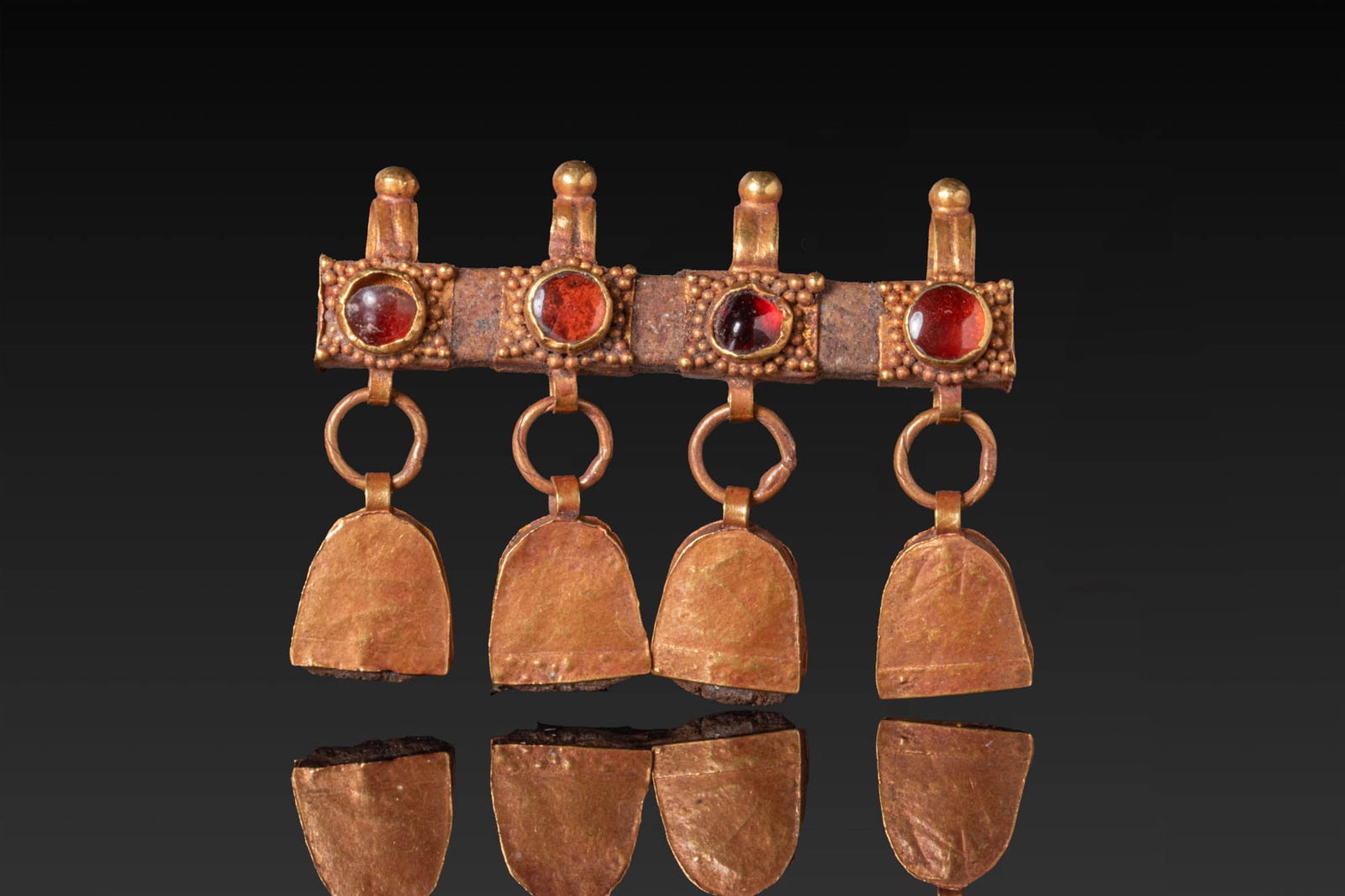 ROMAN HIGH KARAT GOLD PENDANT WITH RED GARNETS AND DANGLES: Ca. AD 100 - 300. A gold pendant formed as a horizontal bar with four rectangular sleeve elements of thin sheet, each with a granulated face and a circular cell set with a garnet cabochon, with a susp