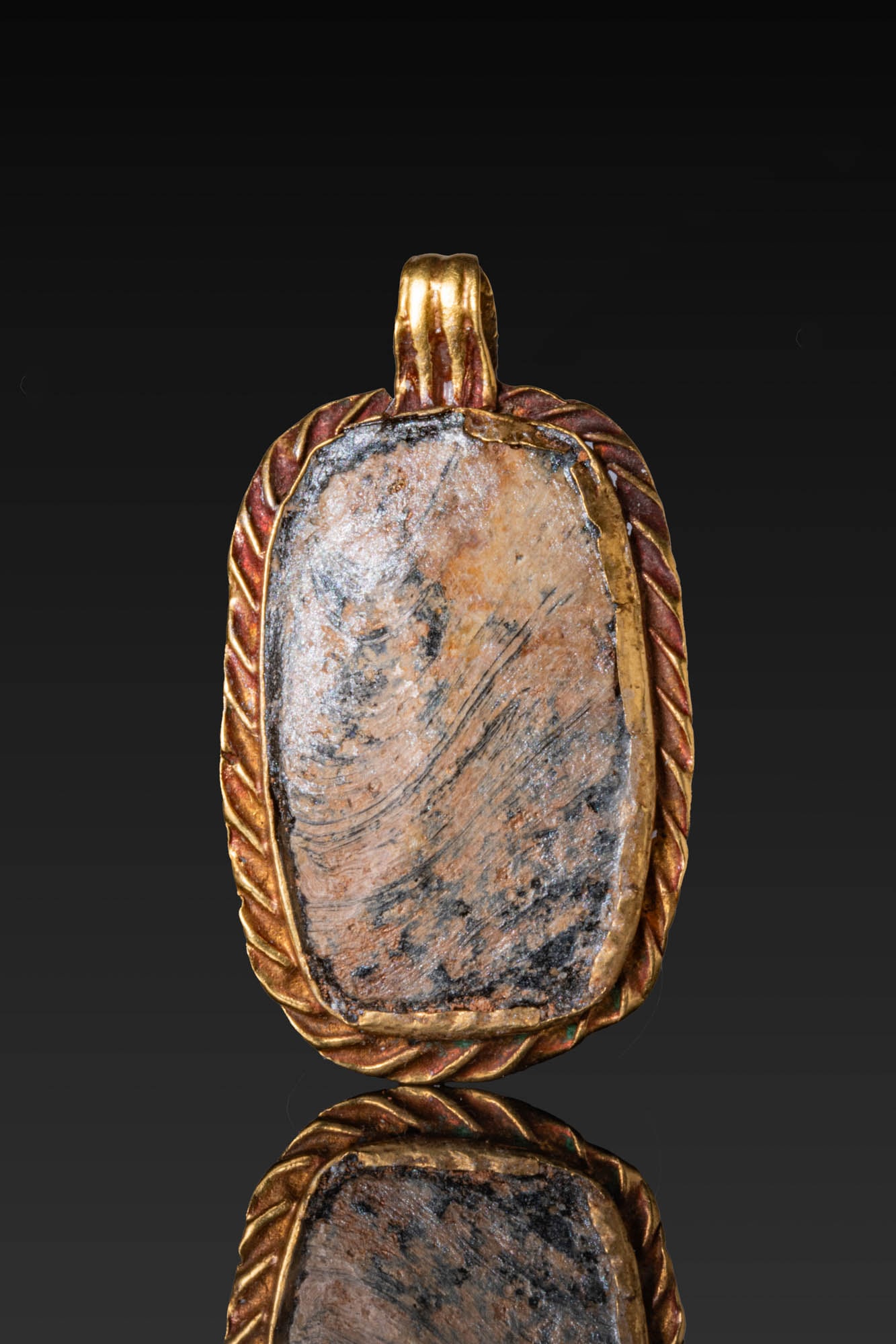 LARGE ROMAN HIGH KARAT GOLD PENDANT WITH GLASS CABOCHON: Ca. AD 100 - 300. A gold pendant formed as a rectangular mount with rounded corners, with an outer border of short ribbing framing a plain bezel set with a large glass cabochon. A broad, ribbed suspen