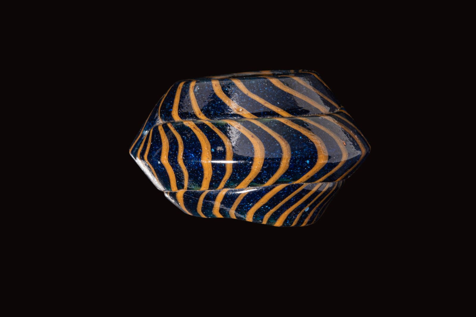 LARGE ROMAN MOSAIC GLASS BEAD: Ca. AD 1 - 300. A dark blue bead with a broad, central carinated band, the body decorated with undulating trails in opaque yellow. Size: 48mm x 31mm; Weight: 61g Provenance: Prince collection, 1990s-2