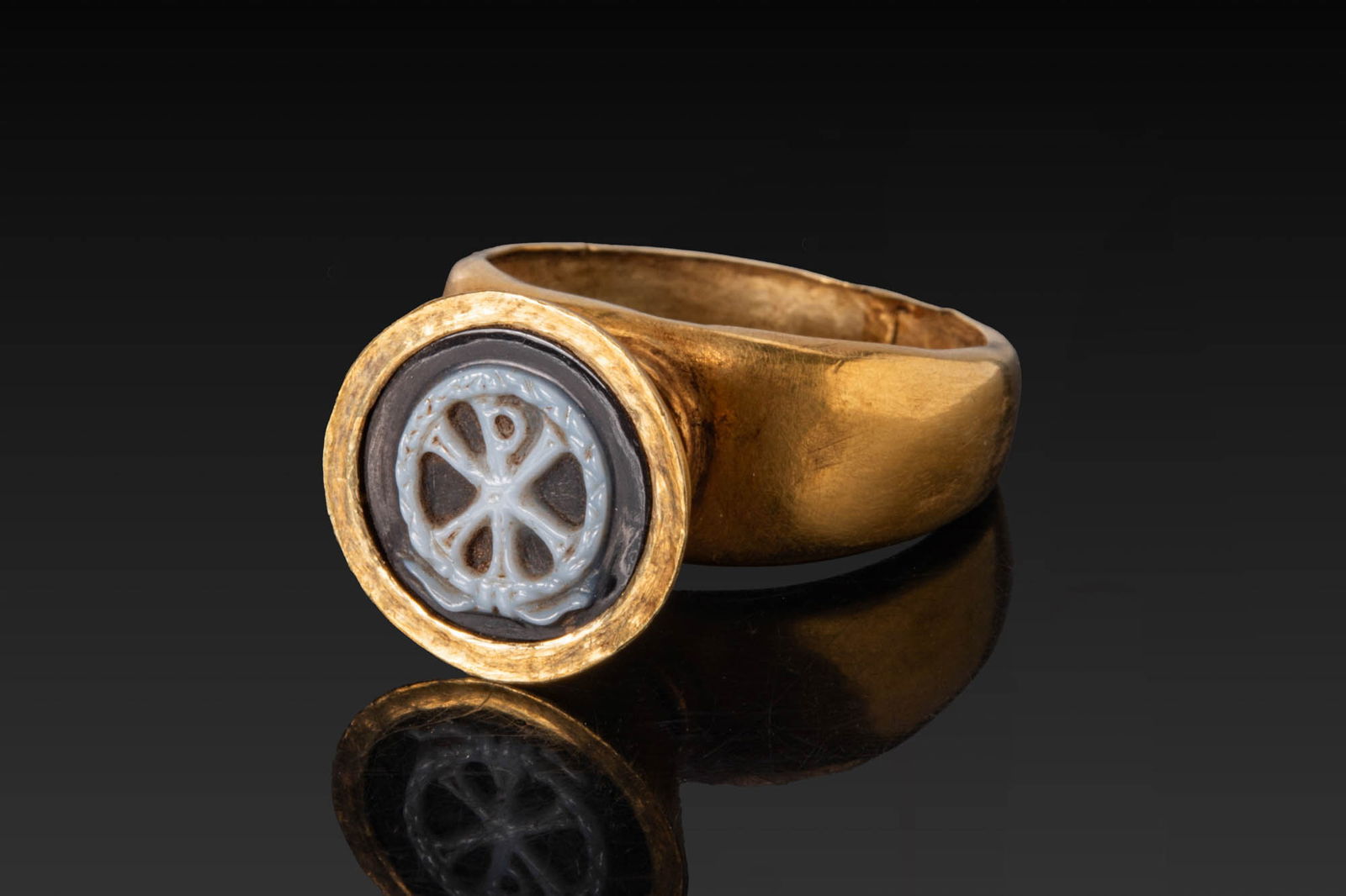 BYZANTINE HIGH KARAT GOLD RING WITH HIGH BEZEL AND AGATE CAMEO WITH CHI-RHO MONOGRAM: Ca. AD 400 - 600. A gold ring with a broad tapering hoop expanding to a high, conical bezel with a narrow plain rim, set with a round agate cameo carved with a Chi-Rho monogram within a wreath. For si