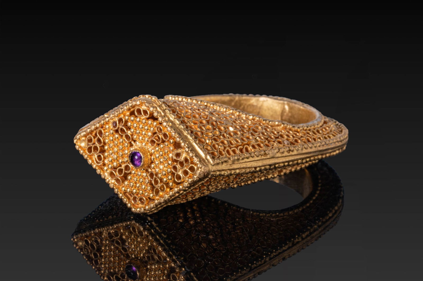 STUNNING BYZANTINE BISHOP'S OPENWORK HIGH KARAT GOLD RING WITH CROSS AND AMETHYST CABOCHON: Ca. AD 500 - 700. A gold ring with a tall bezel framed by beaded wire and filled with openwork scrolls enclosing a granulated cross, centred by an amethyst cabochon. The shoulders and shank with match