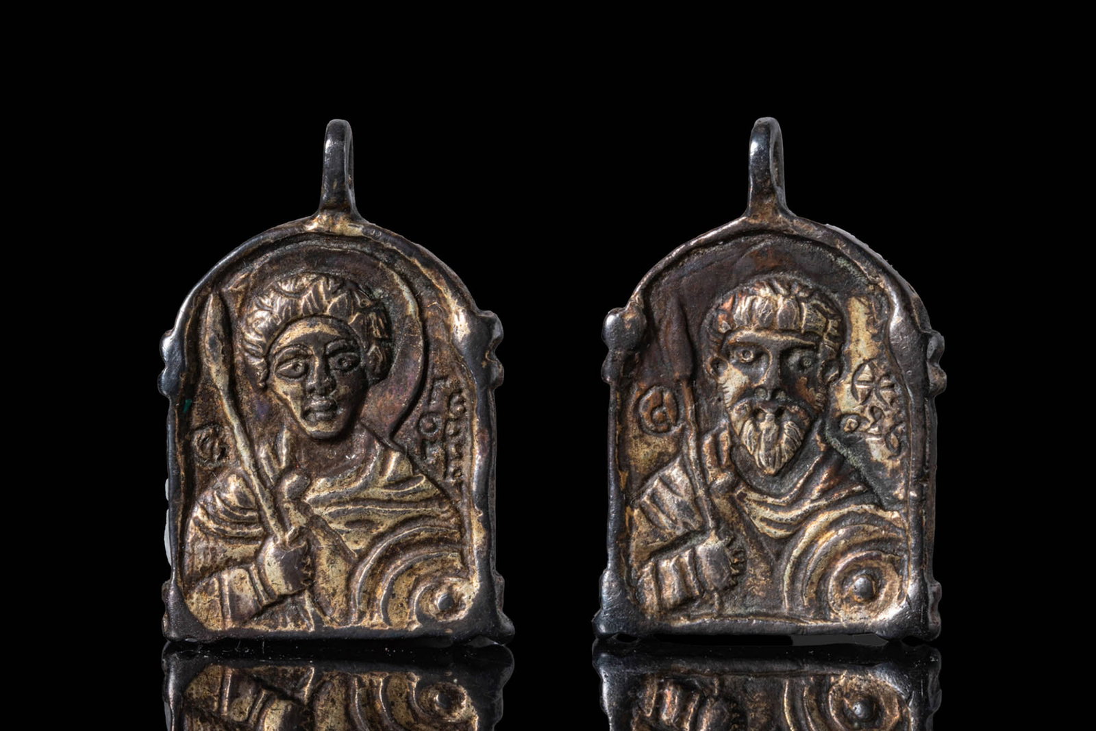 BYZANTINE SILVER-GILT PENDANT WITH ST DEMETRIUS AND ST THEODORE: Ca. 1100. A silver-gilt rectangular pendant with an arched top and a raised border. The obverse shows Saint Demetrius holding a spear and shield, with a nimbus and Greek inscription within the field.