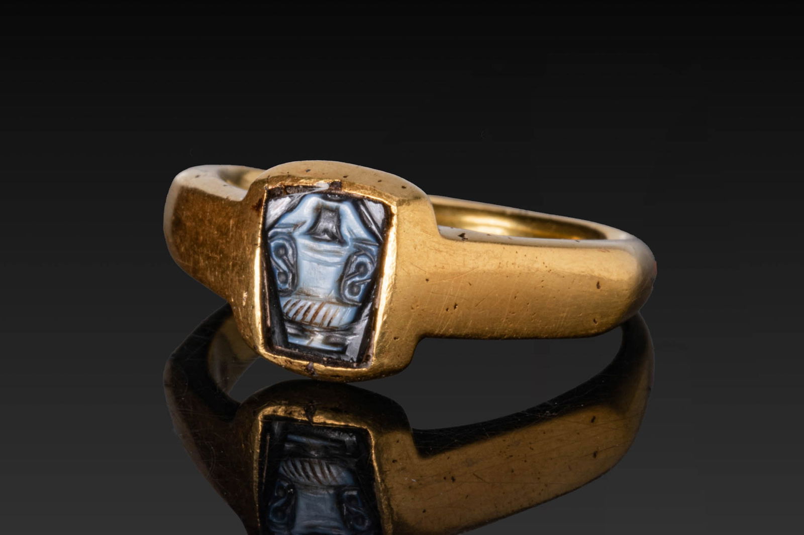 BYZANTINE HIGH KARAT GOLD RING WITH AGATE CAMEO OF DOVES ON AN AMPHORA: Ca. AD 500. A gold ring with a deep bezel frame and angular shoulders merging into a plain hoop, mounted with an agate cameo carved with two doves perched on an amphora with a flaring mouth, two handl