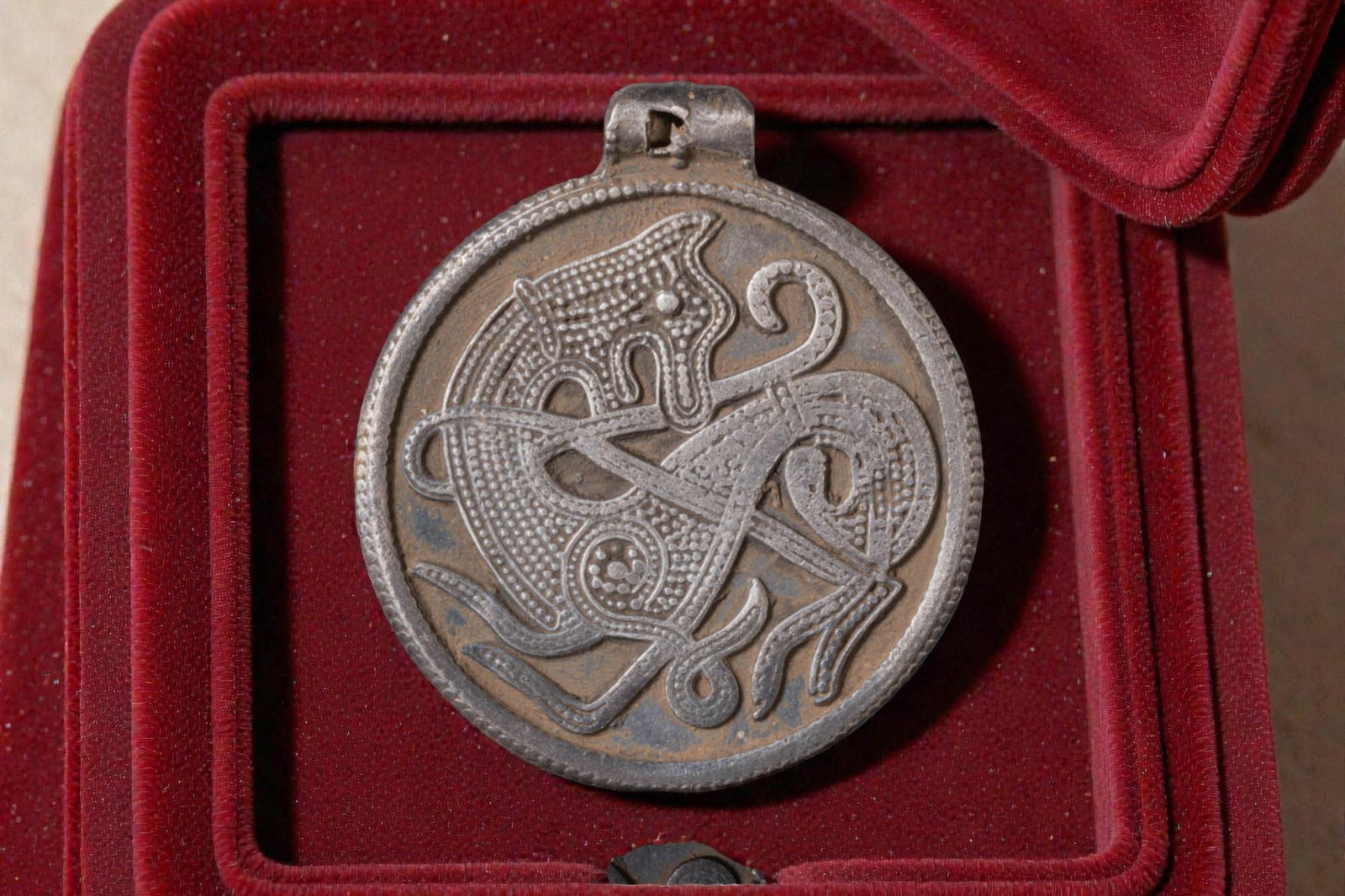VIKING SILVER MEDALLION WITH MYTHOLOGICAL ANIMAL: Ca. AD 800 - 900. A silver medallion, the obverse with a mythological animal in low relief, its elongated sinuous body filled with dense granulation, framed by a narrow raised border. An integral susp