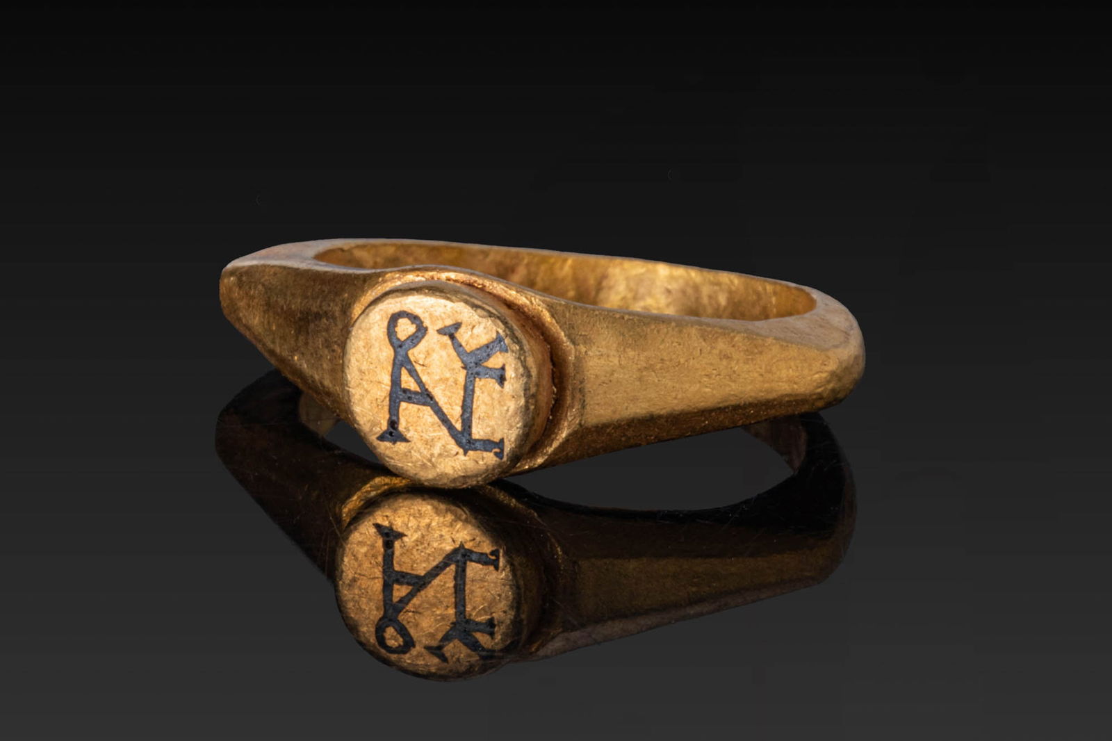 BYZANTINE HIGH KARAT GOLD AND NIELLO RING WITH MONOGRAM: Ca. AD 400 - 600. A gold ring with a tapering hoop of angular profile, faceted shoulders and a circular bezel inlaid in niello with a monogram formed of interlaced letters. For similar see: The Britis