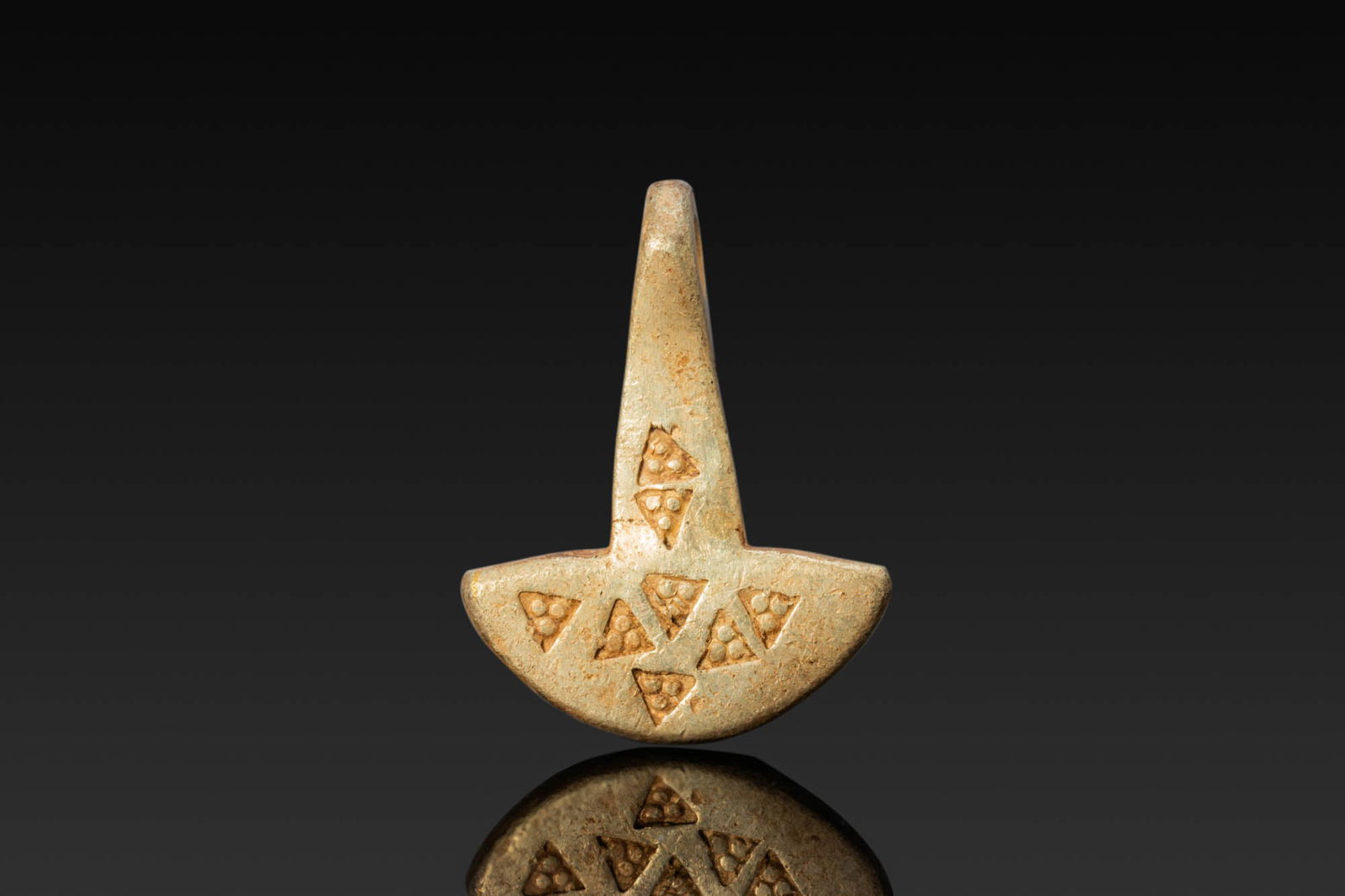 RARE VIKING HIGH KARAT GOLD MJOLNIR PENDANT WITH STAMPED DECORATION: Ca. AD 900 - 1100. A gold hammer-shaped pendant with a tall, tapered shaft and a suspension loop above a broad, crescent-shaped head. Both faces are stamped with an irregular arrangement of triangular