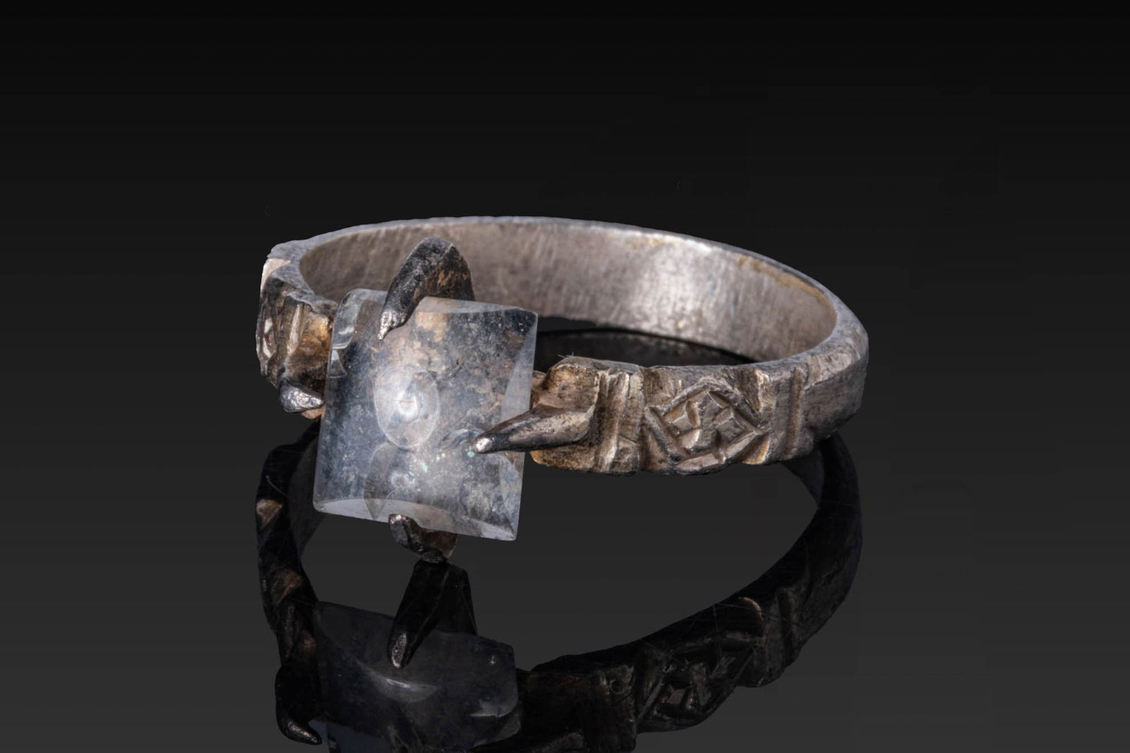 MEDIEVAL SILVER RING WITH PYRAMIDAL QUARTZ GEM: Ca. AD 1200 - 1400. A silver ring with a slender faceted hoop of D-section, the shoulders engraved with lozenges within transverse borders. A bezel with four claws supports a square quartz gem. Size: