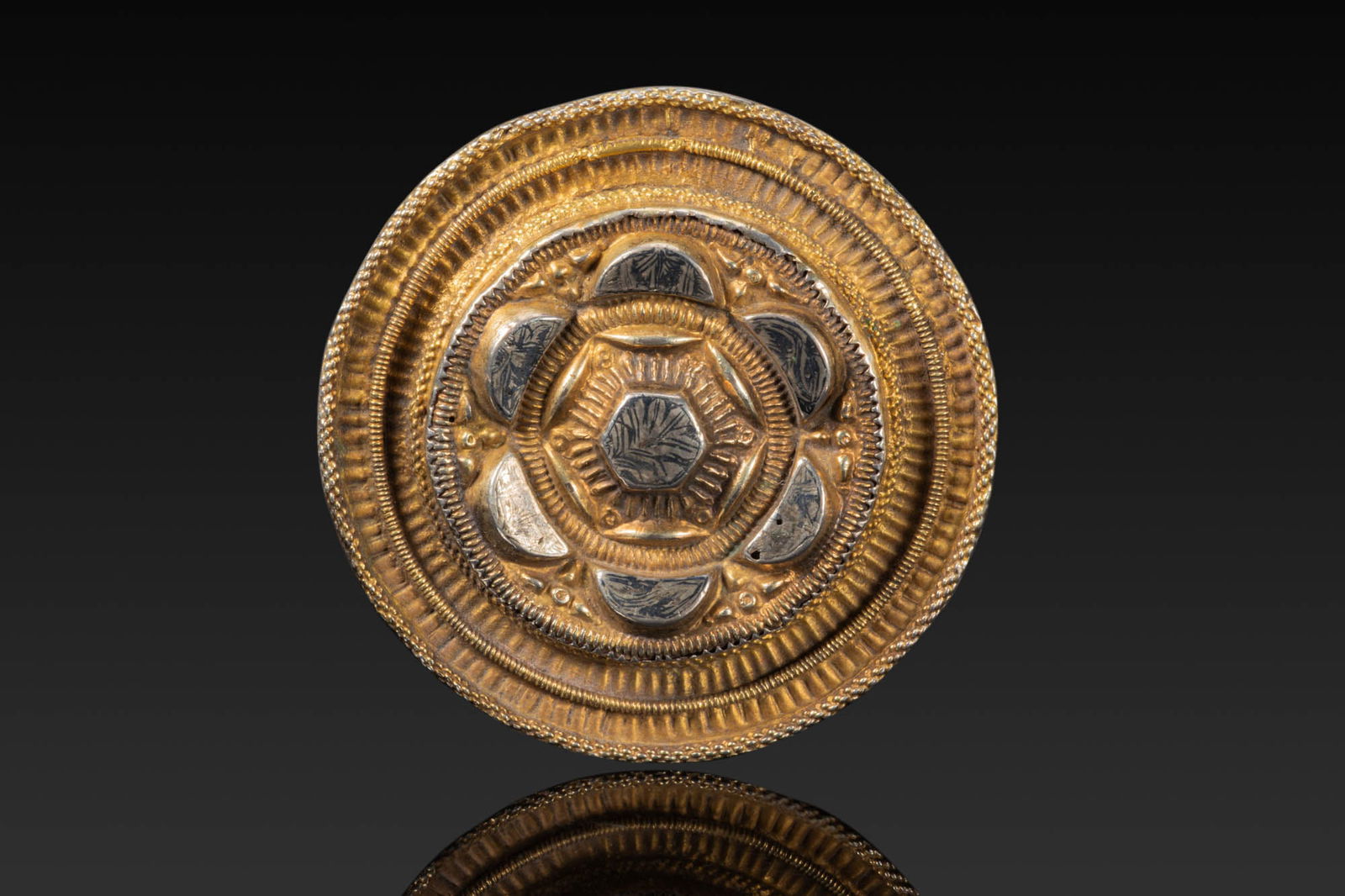 BRITISH TUDOR SILVER-GILT HAT APPLIQU?: Ca. AD 1500 - 1600. A circular silver-gilt hat appliqu? with concentric bands of geometric ornament. The centre is set with six semicircular silver plaques inlaid with black niello, arranged around a