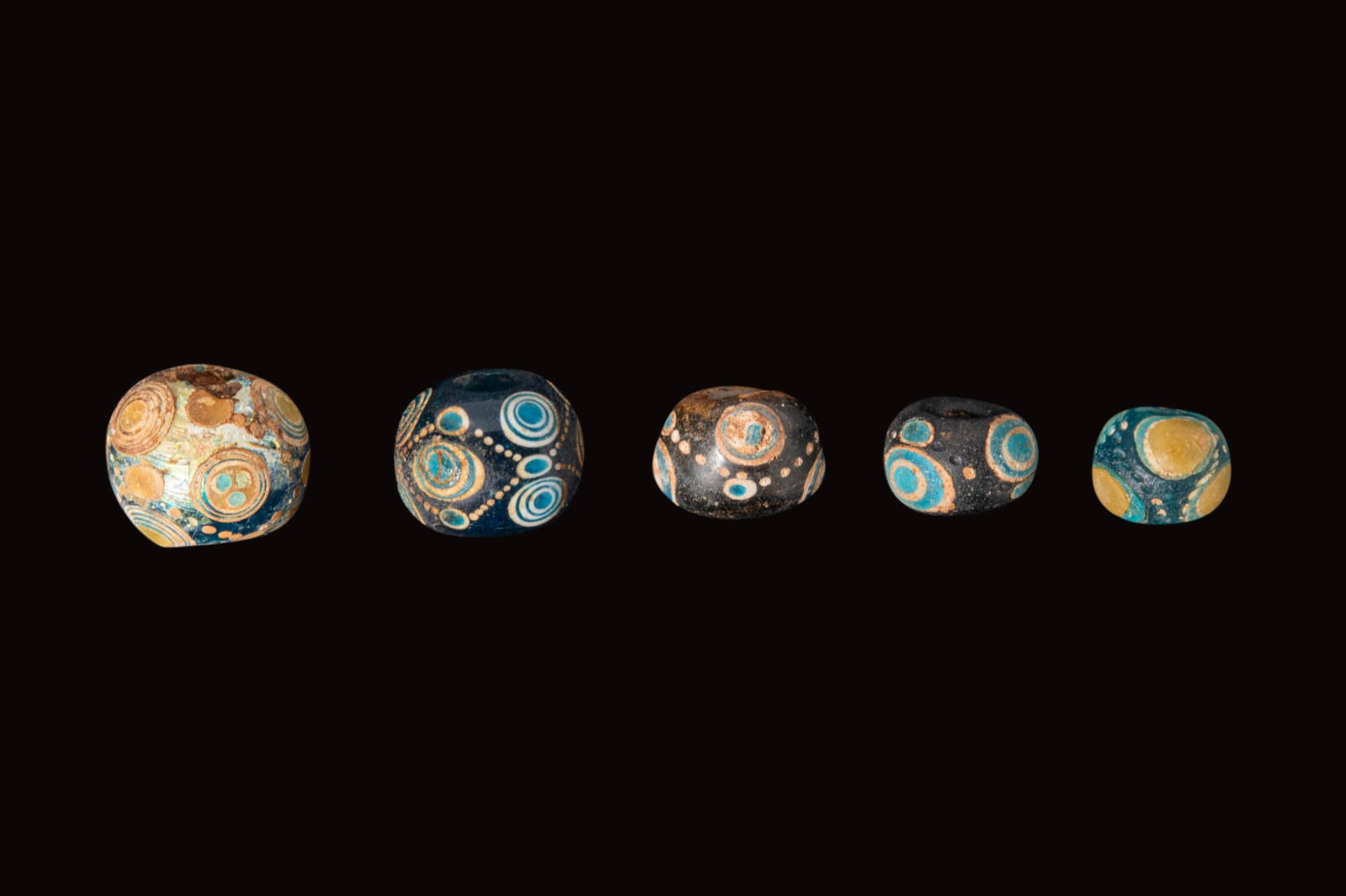 COLLECTION OF ANCIENT CHINESE GLASS EYE BEADS: Ca. 770 - 256 BC. A collection of five beads, each of globular form, in deep blue and black glass with applied concentric eye motifs in turquoise, white and yellow, with dotted trails between the eyes