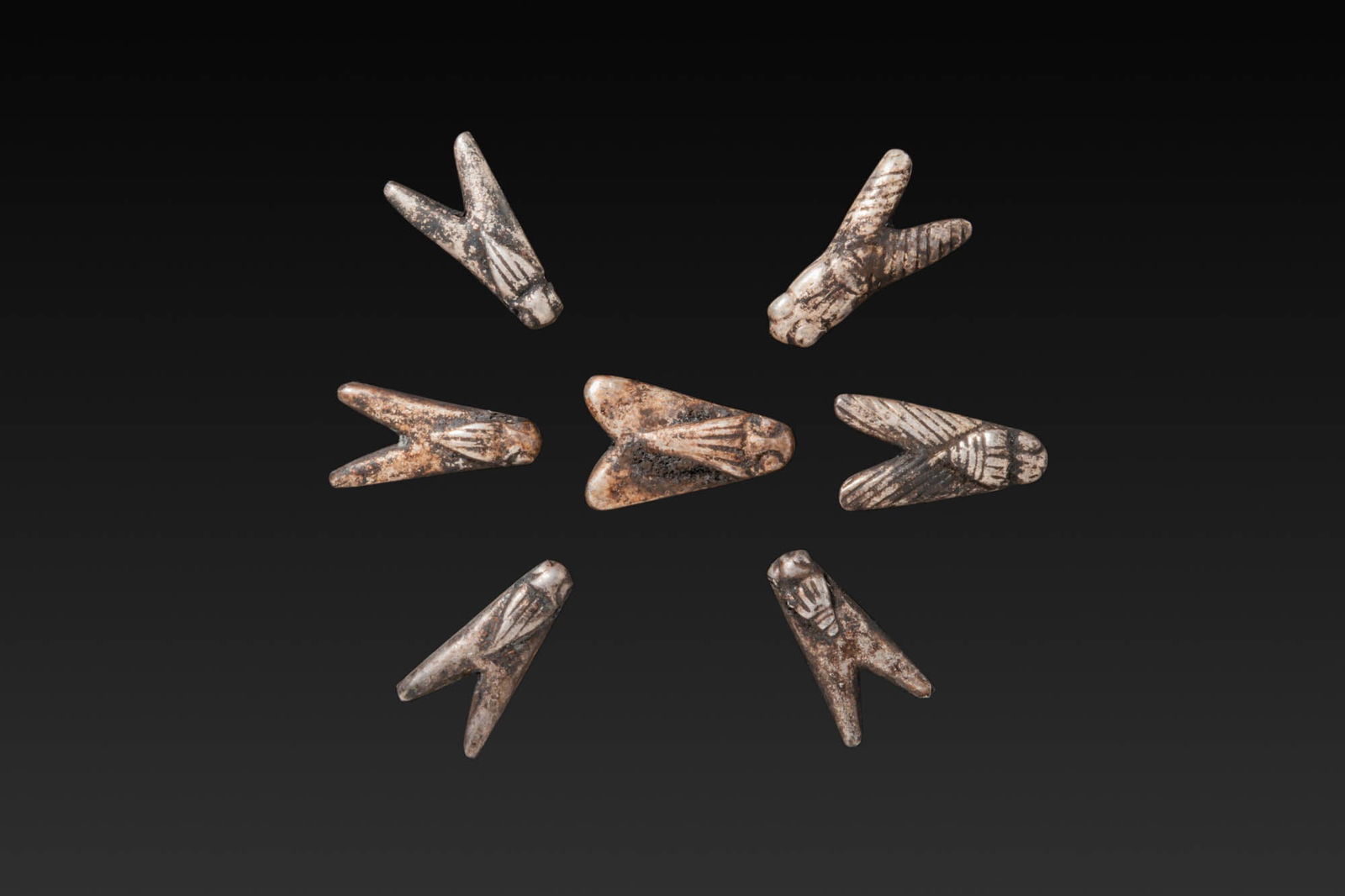 COLLECTION OF EGYPTIAN SILVER FLY AMULETS: New Kingdom, Ca. 1550 - 1069 BC. A collection of seven silver amulets, each cast as a stylised fly with a short body and outspread wings with incised hatching, the head rounded and pierced for suspens