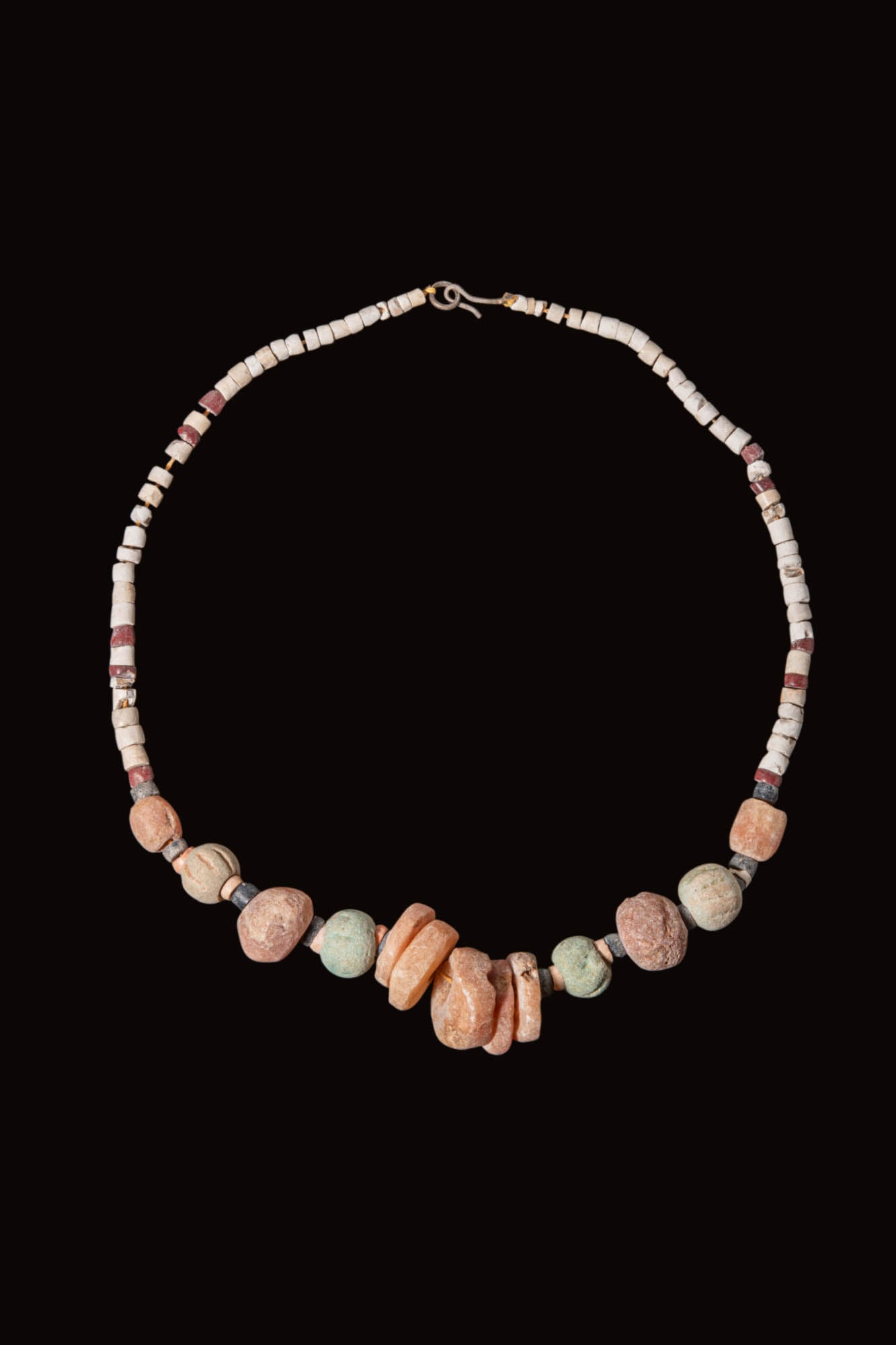 EGYPTIAN FAIENCE AND STONE NECKLACE: New Kingdom to Late Period, Ca. 1550 - 332 BC. A faience and stone necklace strung with white disc beads, interrupted by red and dark spacer beads, and centred on the lower arc by a group of larger st