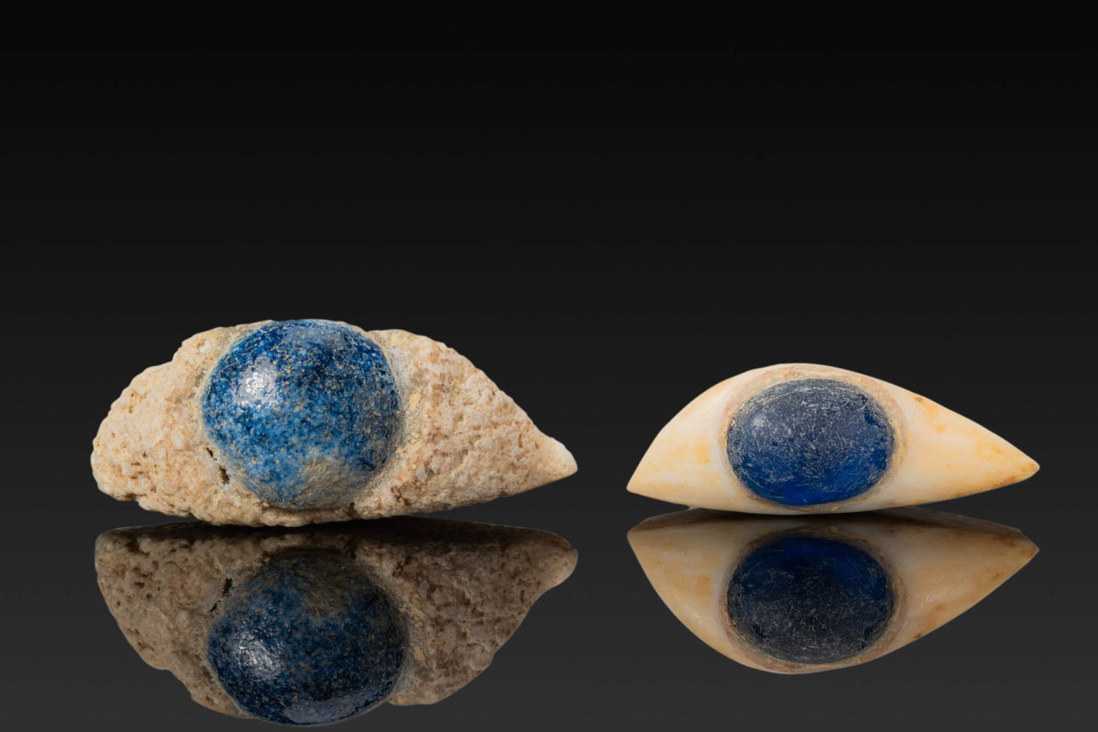 PAIR OF EGYPTIAN STONE AND GLASS EYE INLAYS FROM A MUMMY MASK: New Kingdom to Third Intermediate Period, Ca. 1550 - 664 BC. A pair of eye inlays, each with a white stone sclera and a centrally set circular blue glass iris, the outer edges tapering to pointed corn