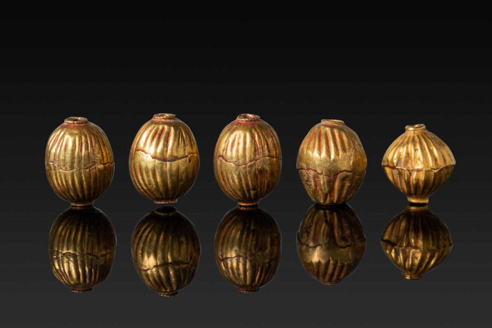 COLLECTION OF GREEK HIGH KARAT GOLD BEADS: Ca. 800 - 600 BC. A collection of five gold beads, including, from left to right: four melon-shaped beads with vertical fluting; and a biconical bead with ribbed body, each with raised collars at the