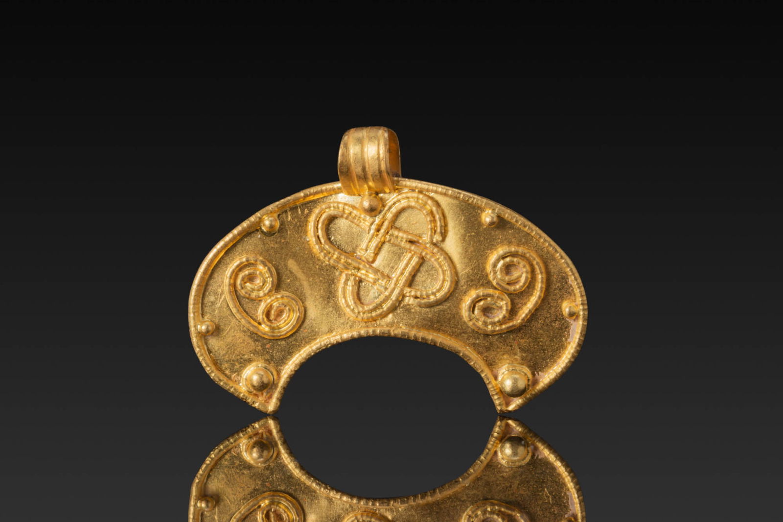 HELLENISTIC LUNAR PENDANT WITH HERCULES KNOT AND HIGH KARAT GOLD PELLETS: Ca. 300 - 100 BC. A gold lunar pendant with a beaded outer border and a plain field decorated with a central Hercules knot in applied wire, flanked by paired scrolls, the perimeter with small pellets