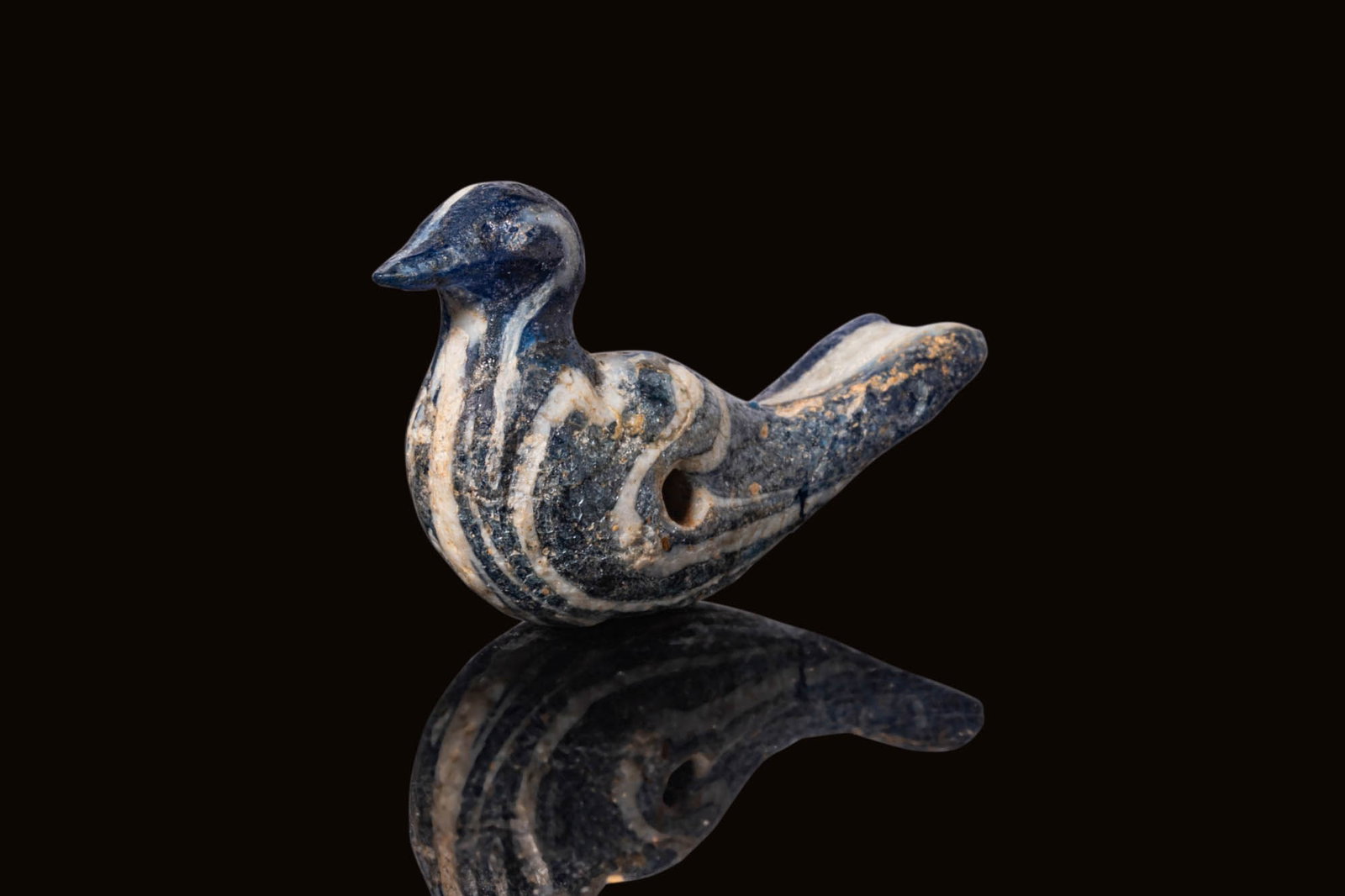 GREEK CORE-FORMED GLASS BIRD-SHAPED PENDANT: Ca. 500 - 300 BC. A dark blue core-formed glass pendant in the form of a stylised bird with a pointed beak, short neck and elongated tail, pierced transversely through the mid-body and decorated with