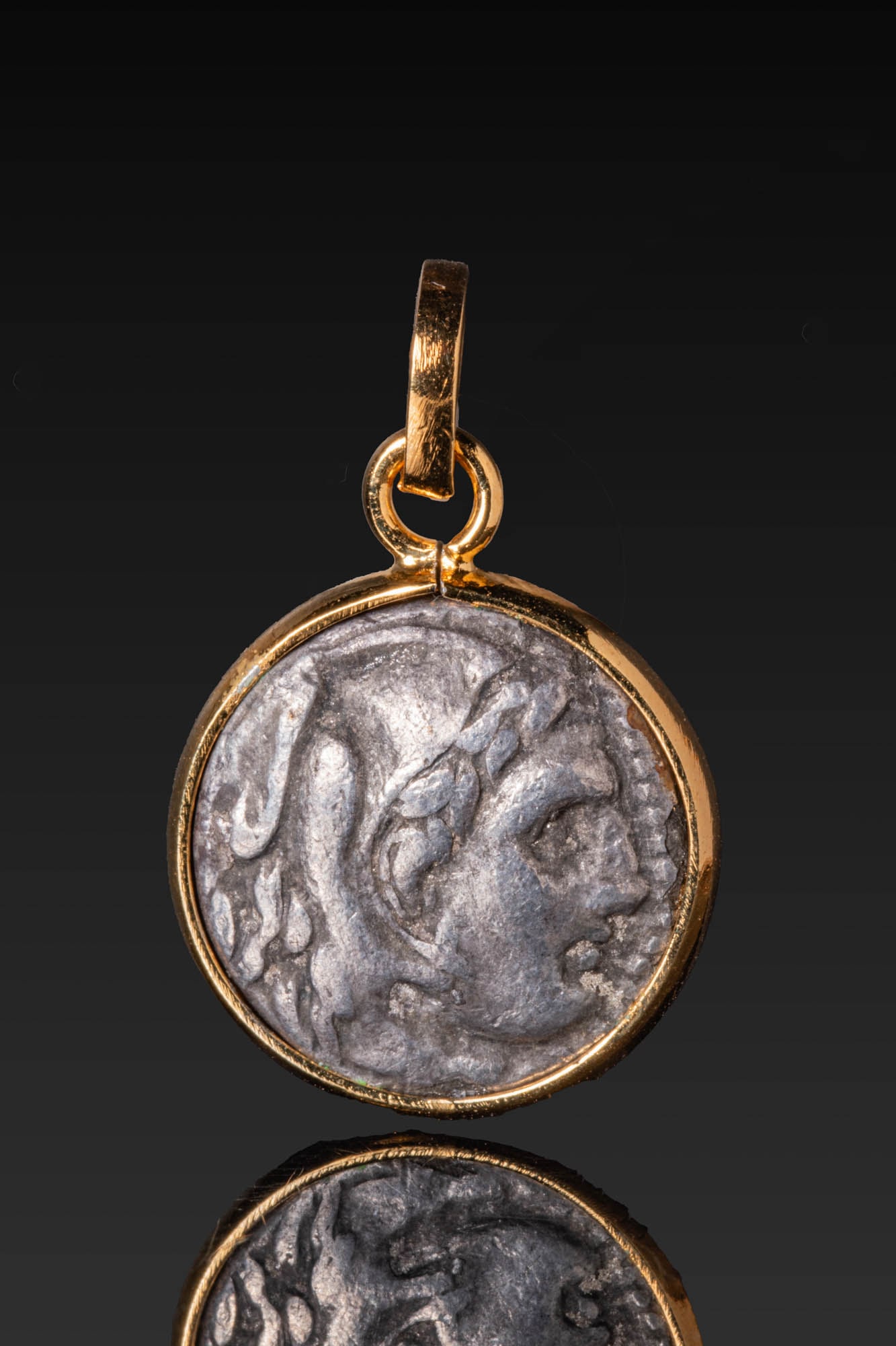 HELLENISTIC SILVER DRACHM OF ALEXANDER THE GREAT IN SILVER-GILT 18KT HIGH KARAT GOLD PENDANT MOUNT: Ca. 336 - 280 BC. A silver drachm of Alexander the Great, the obverse with the head of Herakles facing right, wearing the Nemean lion skin, the paws tied at the neck. The reverse shows Zeus enthroned