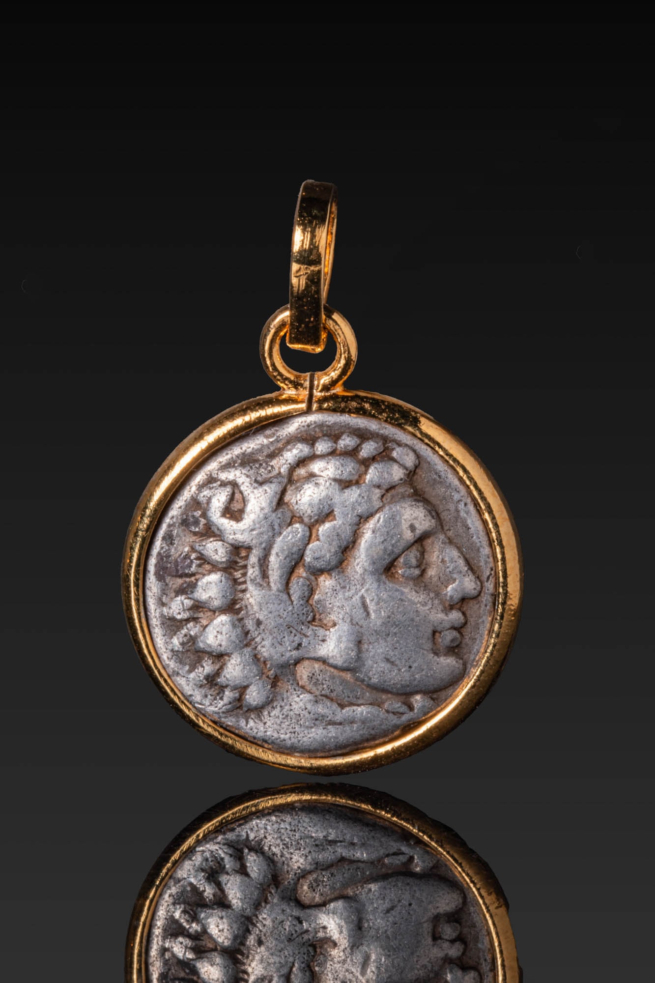 HELLENISTIC SILVER DRACHM OF ALEXANDER THE GREAT IN SILVER-GILT 18KT HIGH KARAT GOLD PENDANT MOUNT: Ca. 336 - 280 BC. A silver drachm of Alexander the Great, the obverse with the head of Herakles facing right, wearing the Nemean lion skin, the paws tied at the neck. The reverse shows Zeus enthroned