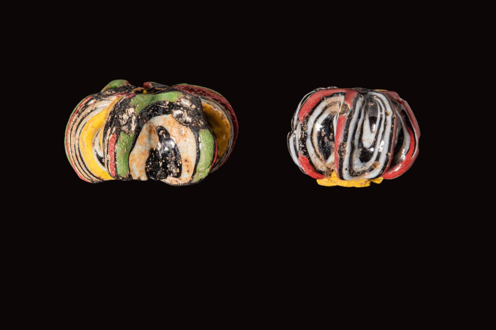 PAIR OF PHOENICIAN GLASS BEADS: Ca. 400 - 200 BC. A pair of glass beads, each a lobed annular bead with polychrome trails in green, red, yellow and white over a black core. Size: 29-39mm x 20-21mm; Weight: 44g Provenance: Prince col