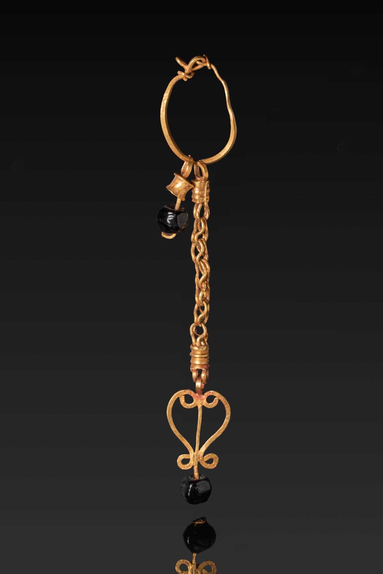 ROMAN HIGH KARAT GOLD EARRING WITH DANGLE AND GEMSTONES: Ca. AD 1 - 300. A gold hoop earring suspending a short pendant comprising a gold collar and an annular bead, and a long interlinked chain ending in an openwork heart-form element with a matching bead