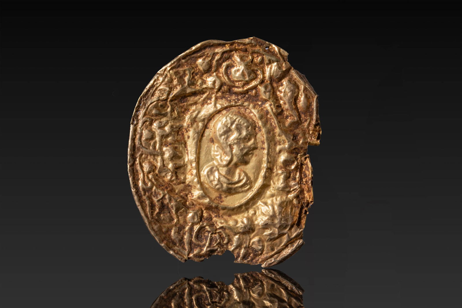LATE ROMAN HIGH KARAT GOLD APPLIQU? WITH PORTRAIT OF JULIA DOMNA: Ca. AD 300 - 500. A repousse gold appliqu?, centred by a medallion with the bust of Julia Domna in right profile, with swept hair and drapery at the shoulders. The portrait is framed by a raised oval