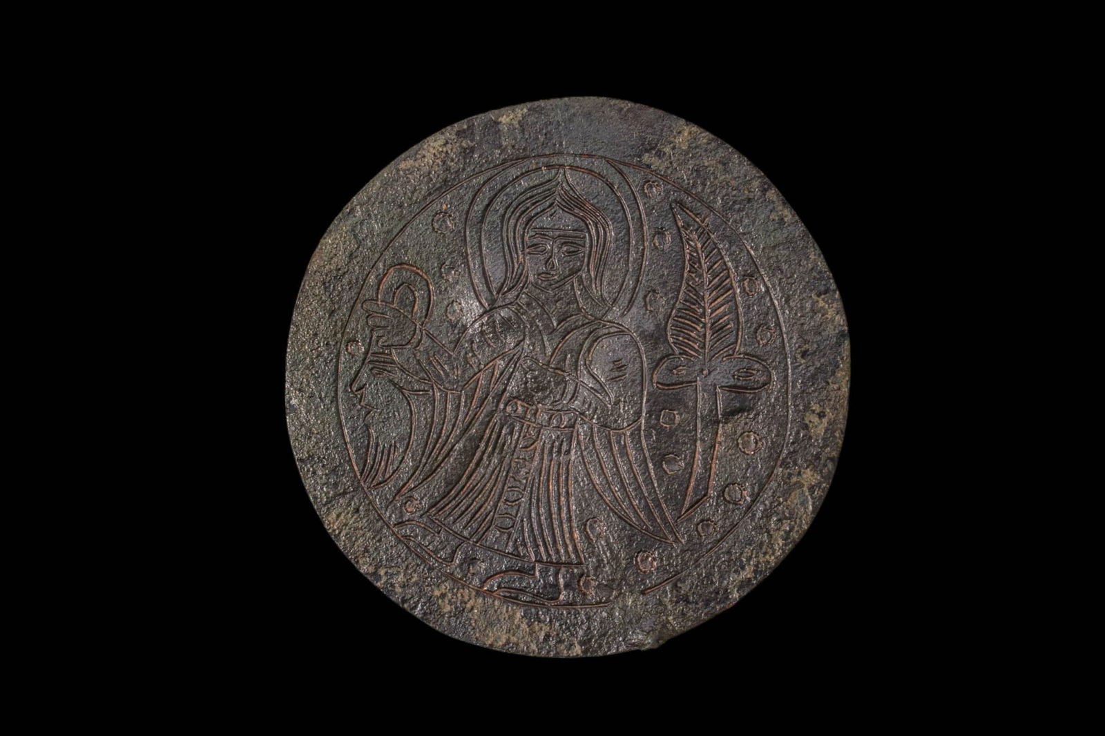 RARE BYZANTINE BRONZE APPLIQU? WITH AN ANGEL HOLDING A MASK: Ca. AD 1000 - 1200. A bronze circular appliqu? with the obverse incised with a standing angel in frontal view, with a nimbus and long hair, holding a mask by the strap. A stylised foliate motif fills
