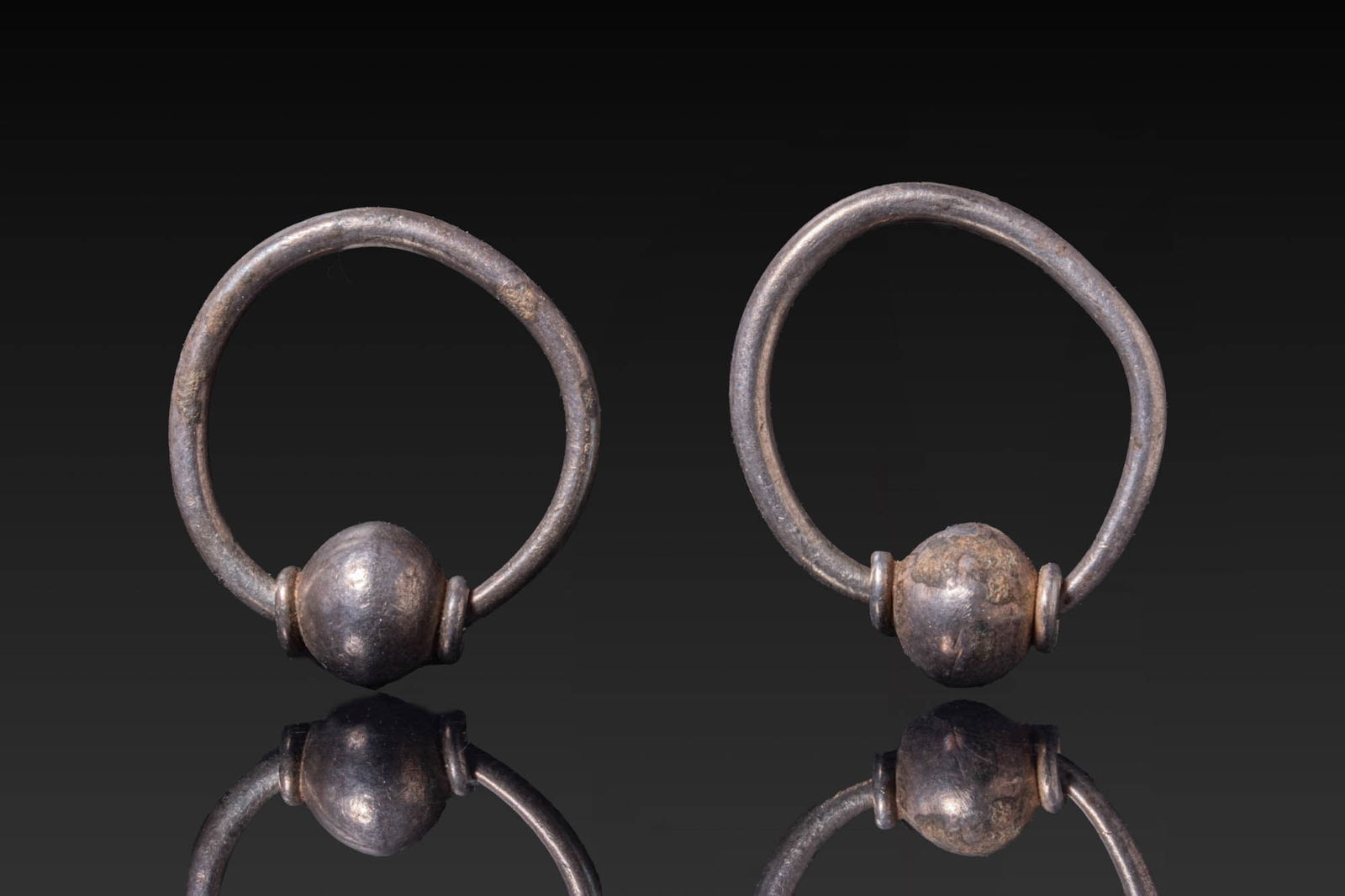 MATCHING PAIR OF BYZANTINE SILVER EARRINGS: Ca. AD 500 - 700. A matched pair of silver hoop earrings, each formed from a plain circular wire hoop threaded with a spherical bead flanked by two small collars. For similar see: A. Bollok, Byzantine