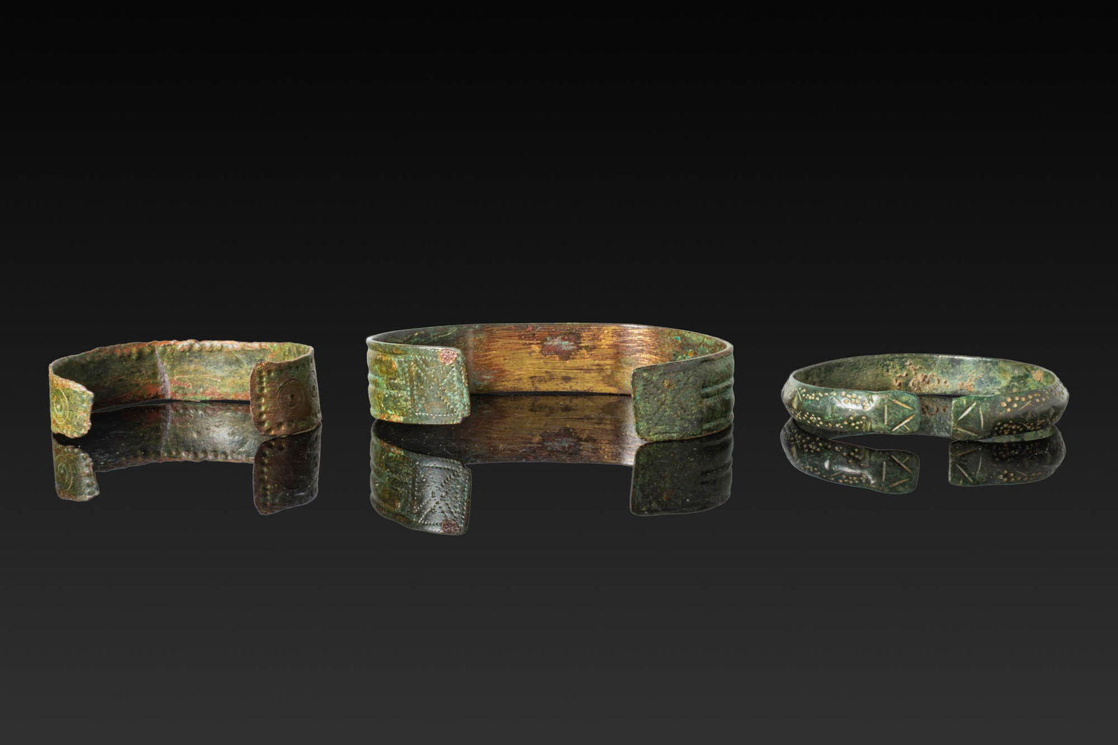 COLLECTION OF VIKING BRONZE BRACELETS: Ca. AD 700 - 900. A collection of three bronze bracelets, including, from left to right: an open cuff of flat-section, the exterior decorated with a band of stamped concentric roundels between punched