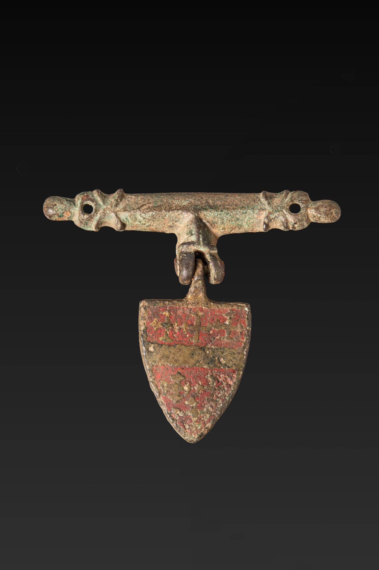 BRITISH MEDIEVAL COPPER ALLOY GILDED AND ENAMELLED SHIELD-SHAPED HERALDIC HORSE HARNESS PENDANT WITH: Ca. AD 1250 - 1400. A copper alloy horse harness pendant, gilded and enamelled, with a transverse bar pierced at either end for attachment and a central hinge supporting a shield-shaped pendant. The s